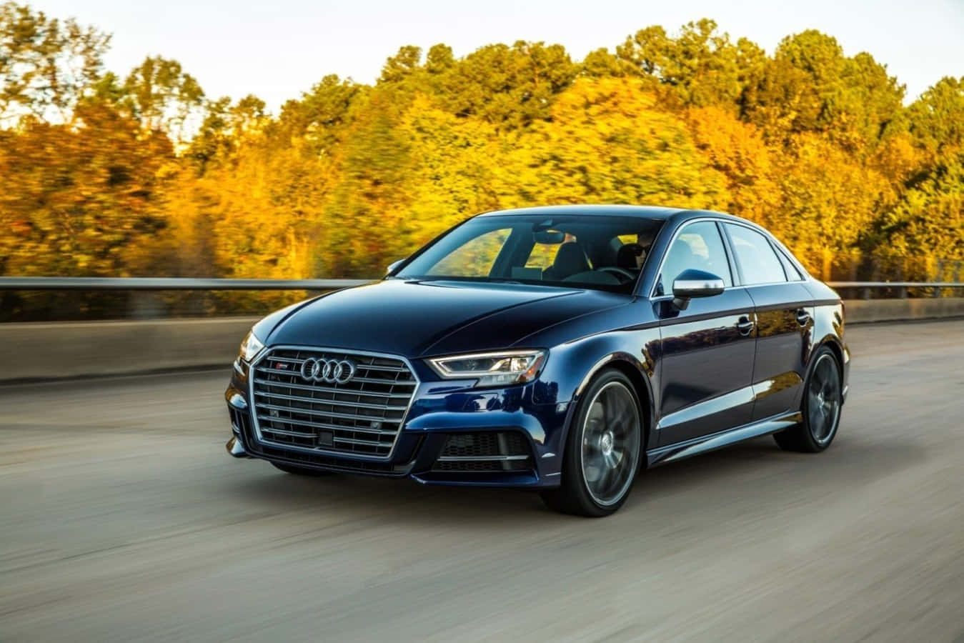 Audi A3 桌布 壁紙 — 一輛時尚的藍色奧迪轎車在道路上疾馳，背景中金色的秋樹模糊不清。
