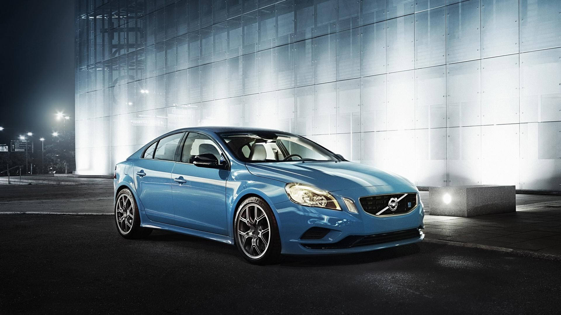Volvo 桌布 壁紙 — 一輛時尚的藍色富豪轎車在夜間於現代玻璃建築前，在聚光燈下閃閃發光。