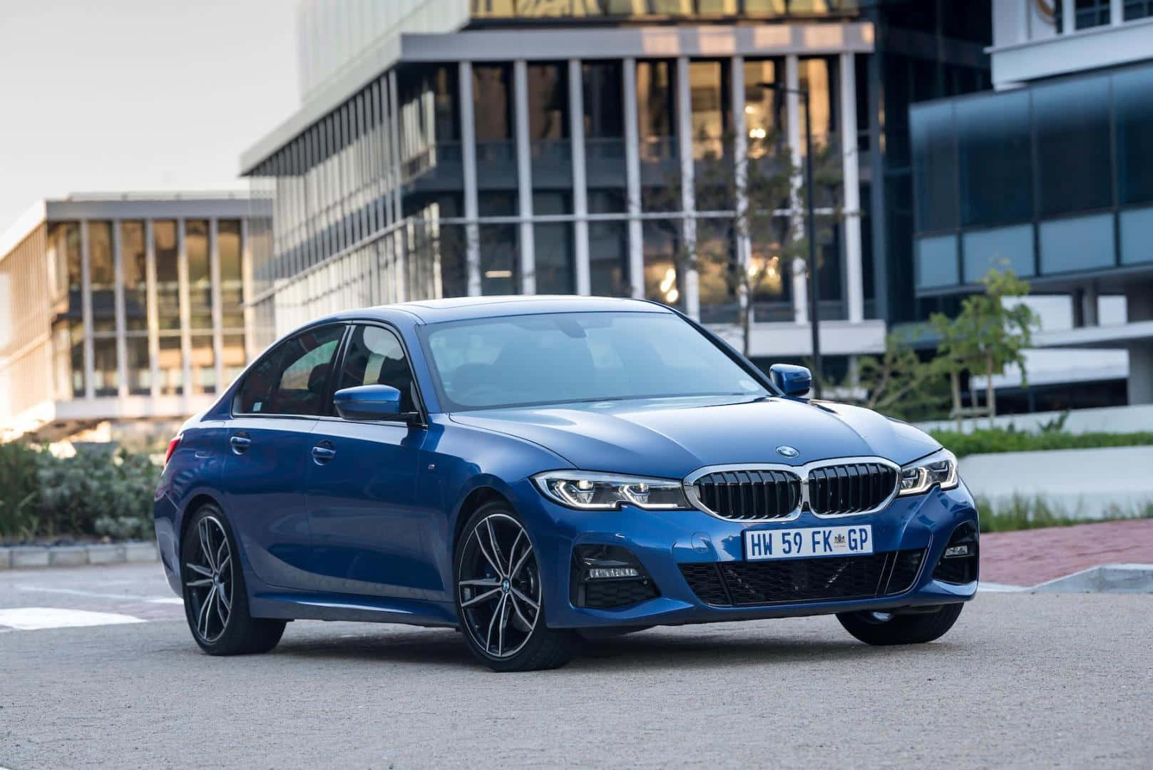 Bmw 3 Series 桌布 壁紙 — 一輛時尚的藍色寶馬轎車停放在現代玻璃建築前，陽光在其拋光表面反射。