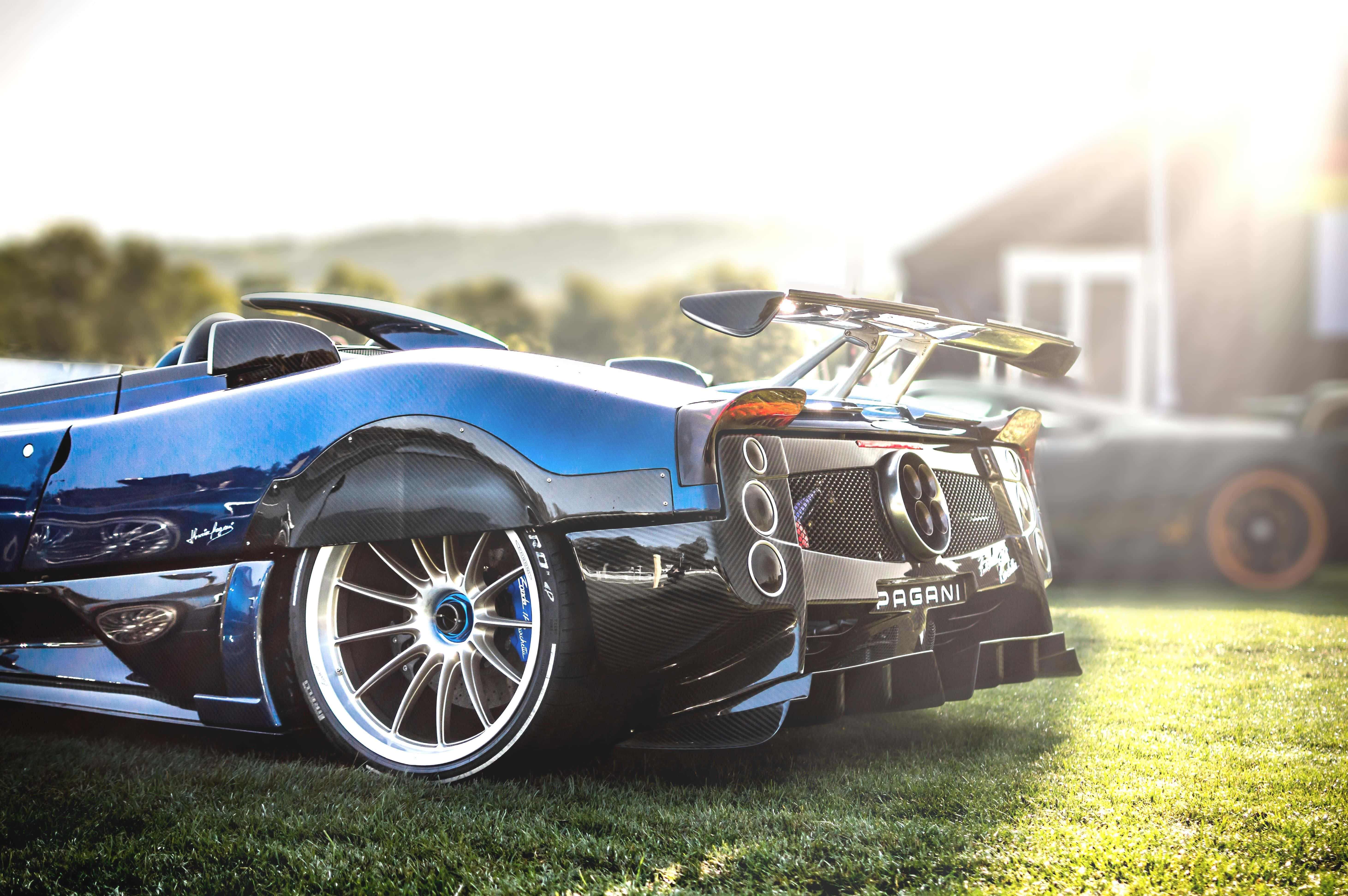 Pagani Zonda Hp Barchetta 桌布 壁紙 — 一輛時尚的藍色帕加尼 Huayra 跑車在金色日出光線下，以模糊的鄉村背景為襯托，在草地上閃閃發光。