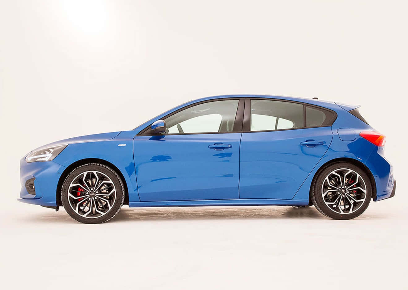 Ford Focus 桌布 壁紙 — 一輛時尚的藍色掀背車，配備黑色合金輪圈和紅色制動卡鉗，在純白色背景上以側面展示。