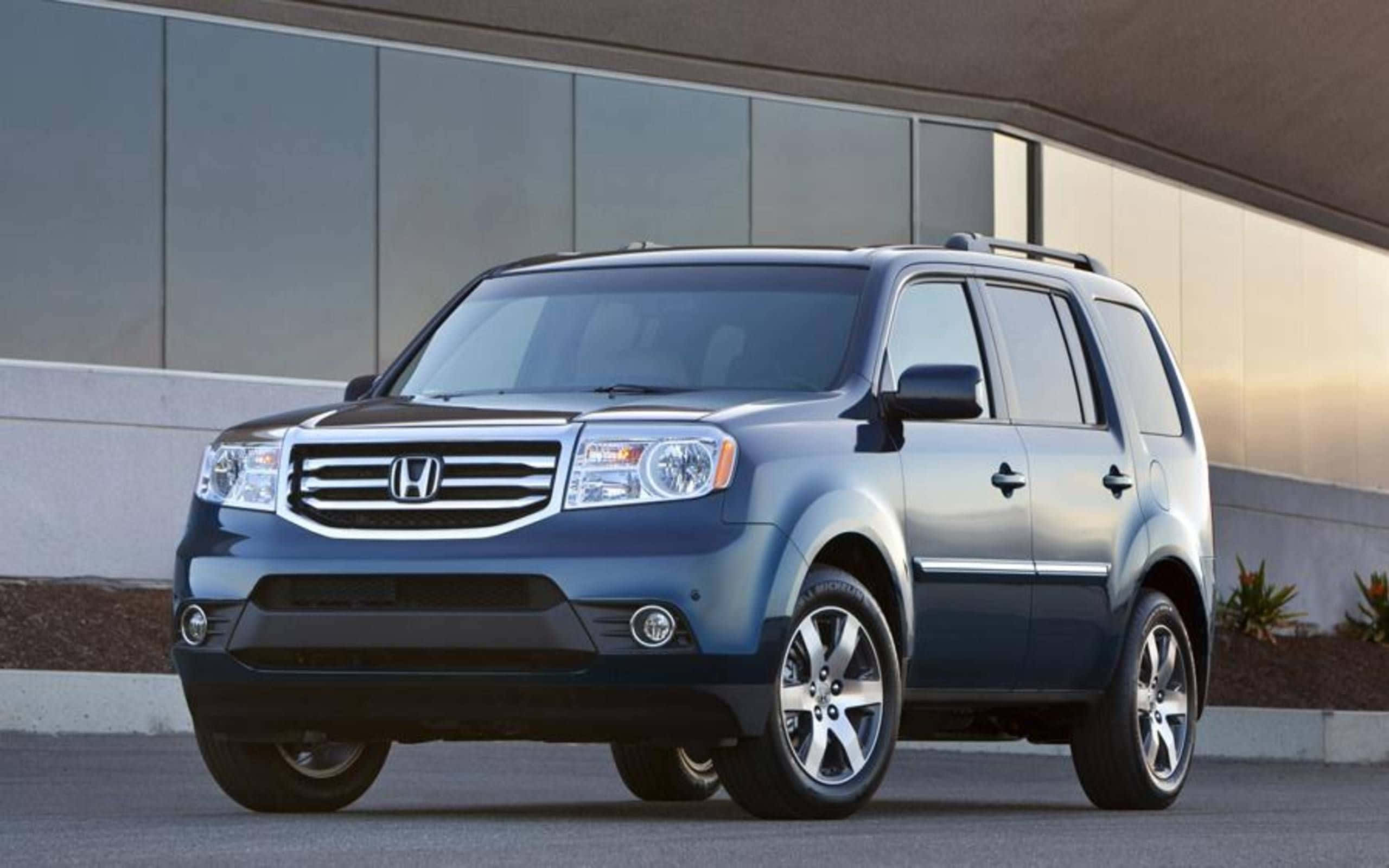 Honda Pilot 桌布 壁紙 — 一輛時尚的藍色本田Pilot SUV停放在現代玻璃建築前，溫暖的陽光投下柔和陰影。