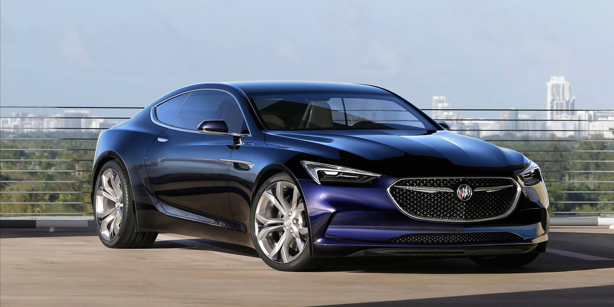 Buick 桌布 壁紙 — 一輛時尚的藍色概念車在日光下閃耀，停泊在可俯瞰遠方摩天大樓城市景觀的屋頂上。
