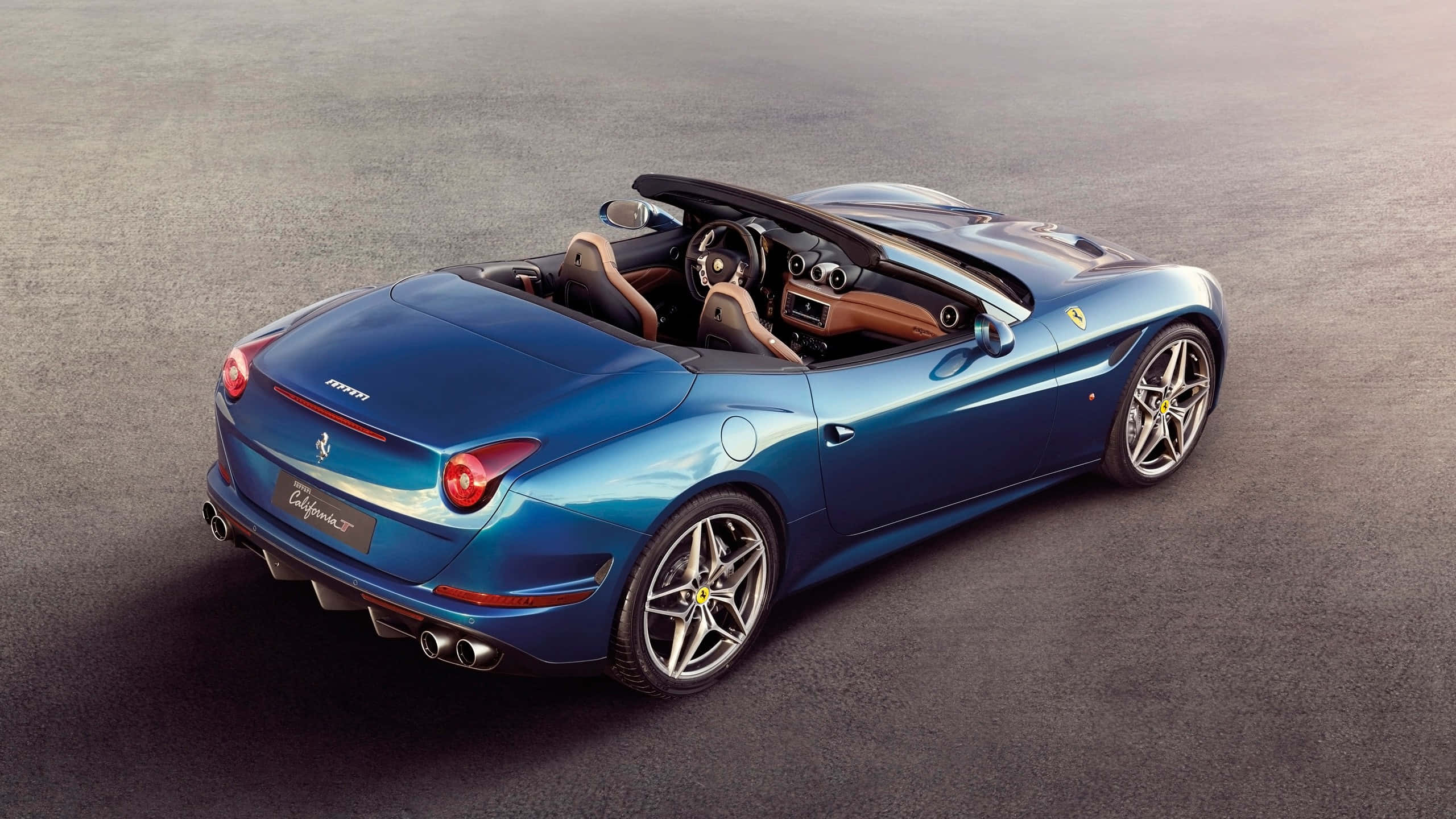 Ferrari California T 桌布 壁紙 — 一輛時尚的藍色法拉利California敞篷跑車，配備棕褐色皮革內飾，停在灰色瀝青路面上。