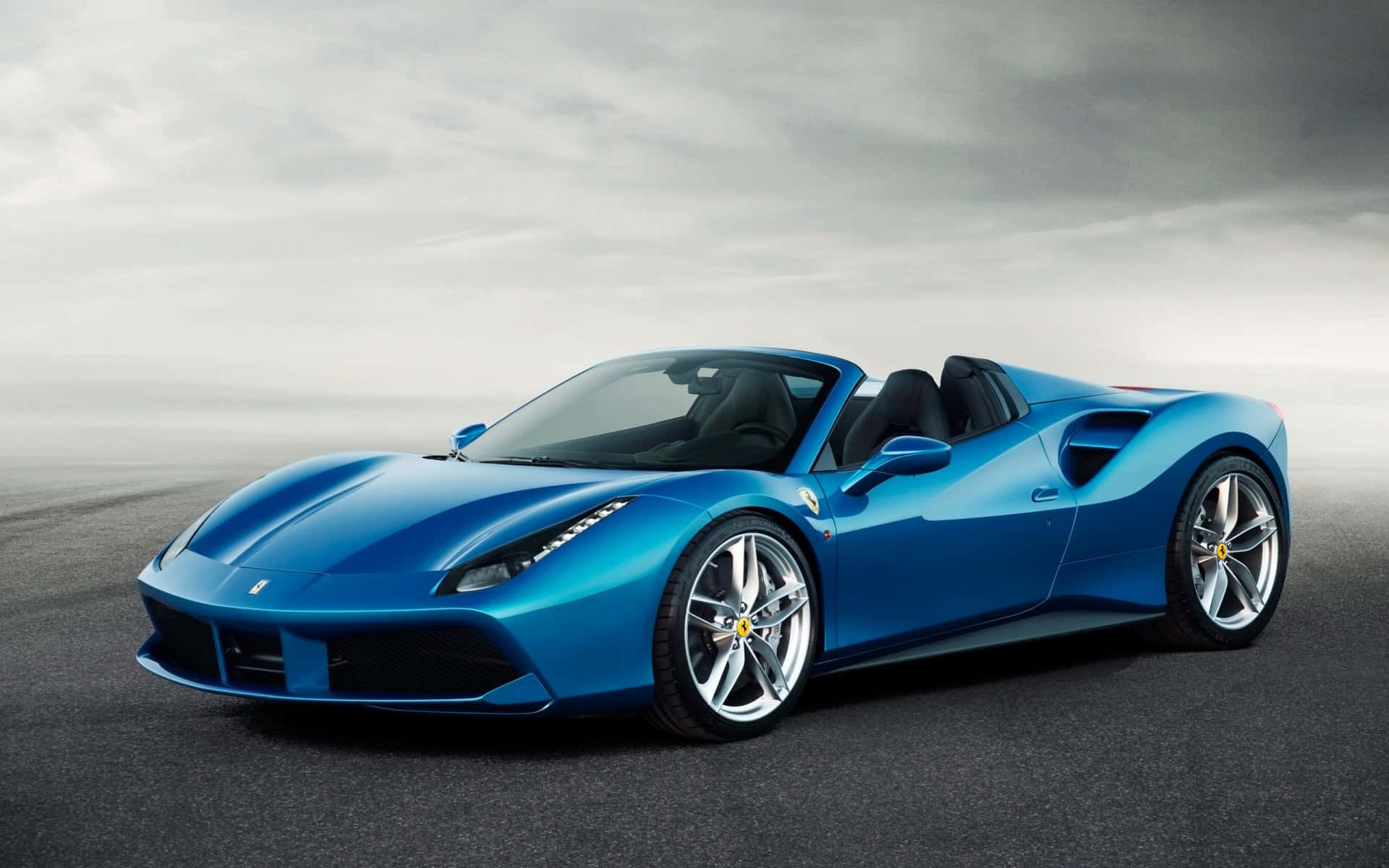 Ferrari 488 Spider 桌布 壁紙 — 一輛時尚的藍色法拉利敞篷跑車在多雲的天空下，在霧濛濛的瀝青路上閃閃發光。