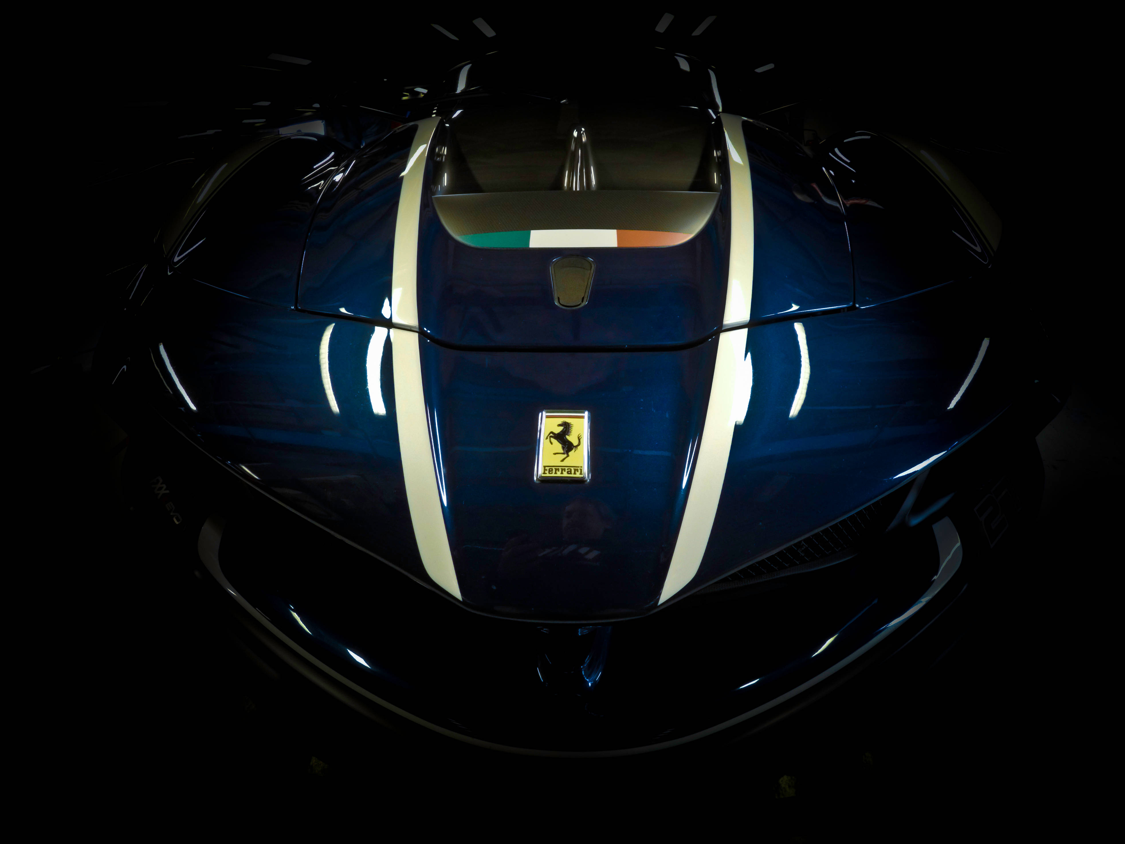ferrari f1 2018 桌布 壁紙 — 一輛時尚的藍色法拉利跑車，帶有白色條紋和義大利國旗點綴，在黑色背景的戲劇性聚光燈下閃耀。