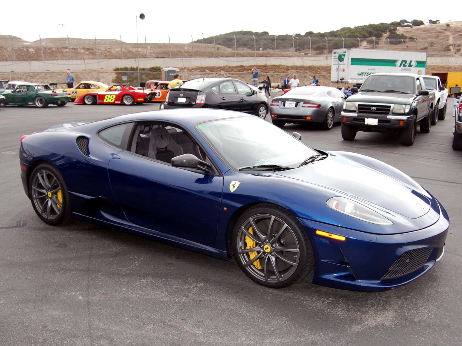 Ferrari F430 桌布 壁紙 — 一輛時尚的藍色法拉利跑車，帶有黃色制動卡鉗，停放在一個被其他車輛和觀眾包圍的停車場中。