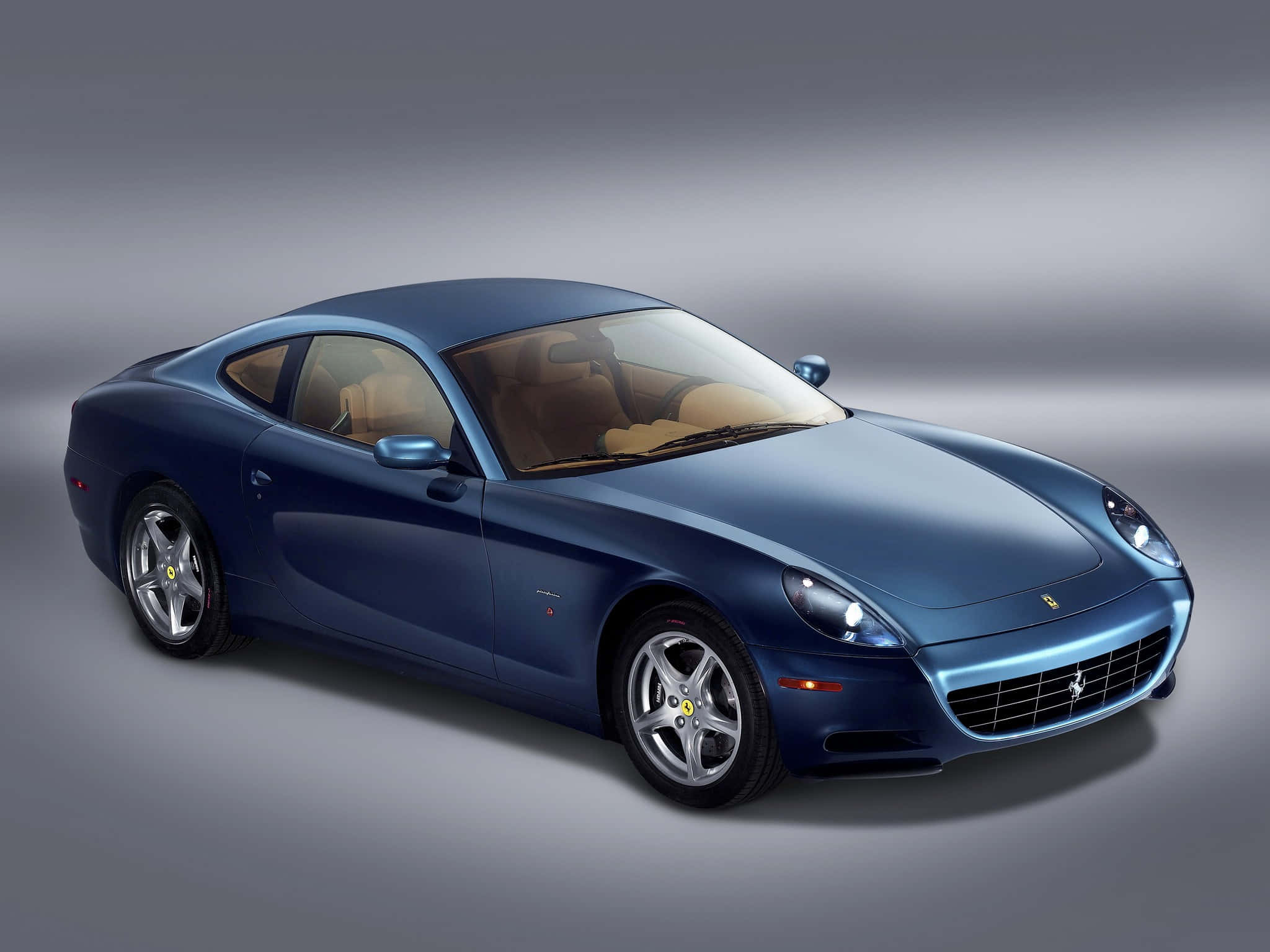 Ferrari 612 Scaglietti 桌布 壁紙 — 一輛時尚的藍色法拉利跑車，配以淺褐色內裝，在柔和漸變燈光的攝影棚環境中展示。