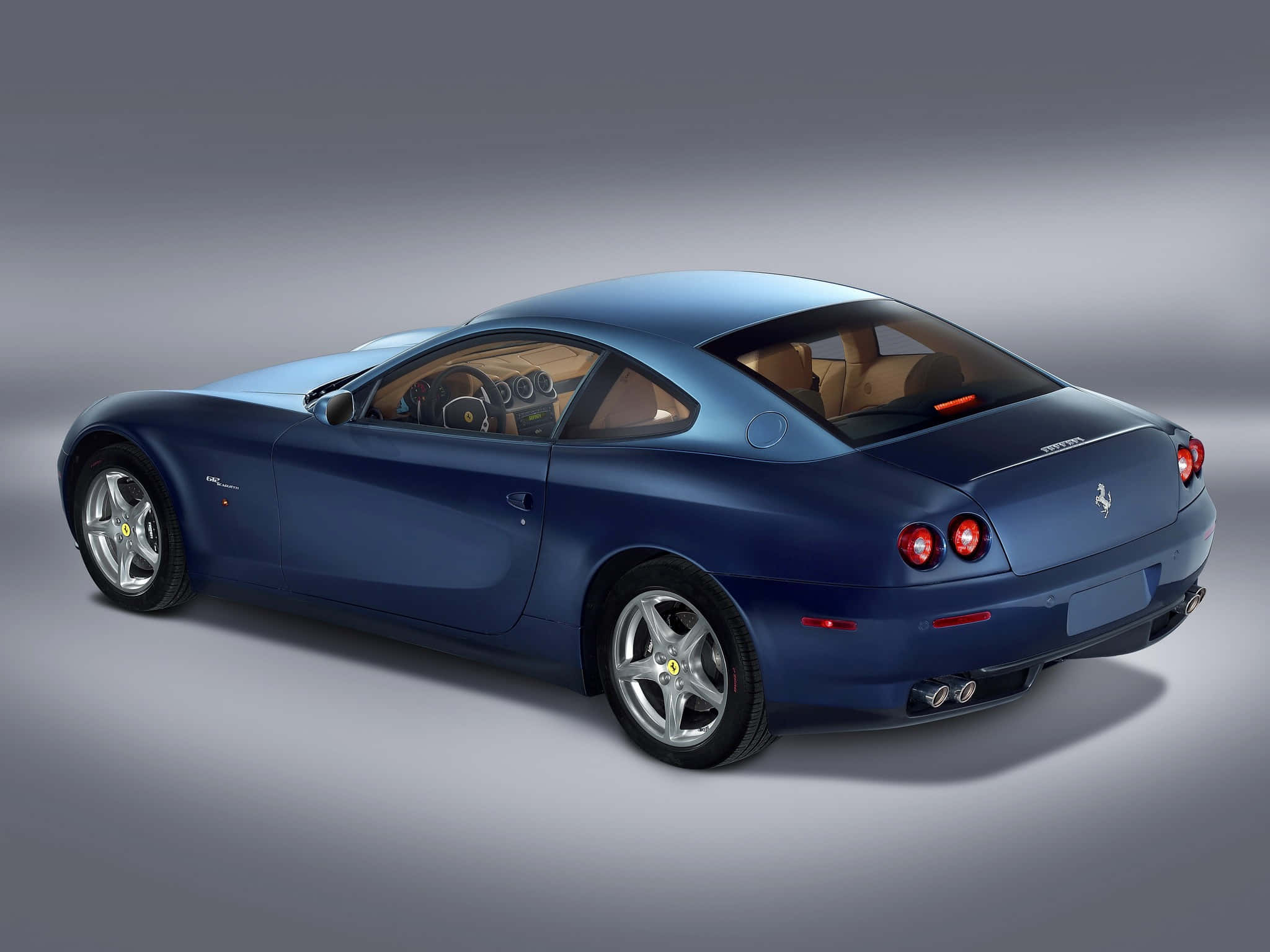 Ferrari 612 Scaglietti 桌布 壁紙 — 一輛時尚的藍色法拉利雙門跑車，配備米色內飾和紅色尾燈，在攝影棚燈光下展示。