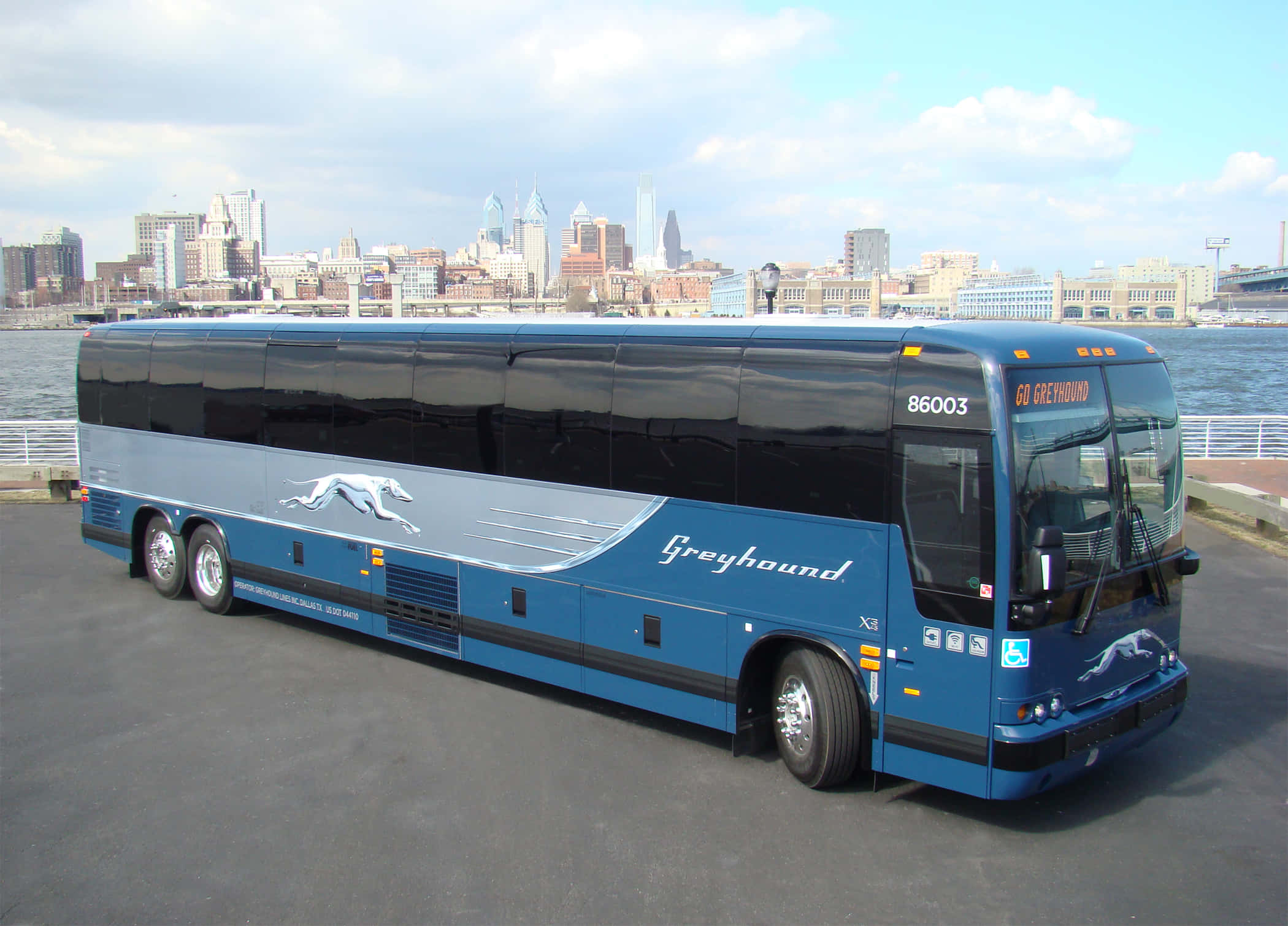 Bus 桌布 壁紙 — 一輛時尚的藍色灰狗巴士停在水邊，背景是城市天際線，天空部分多雲。