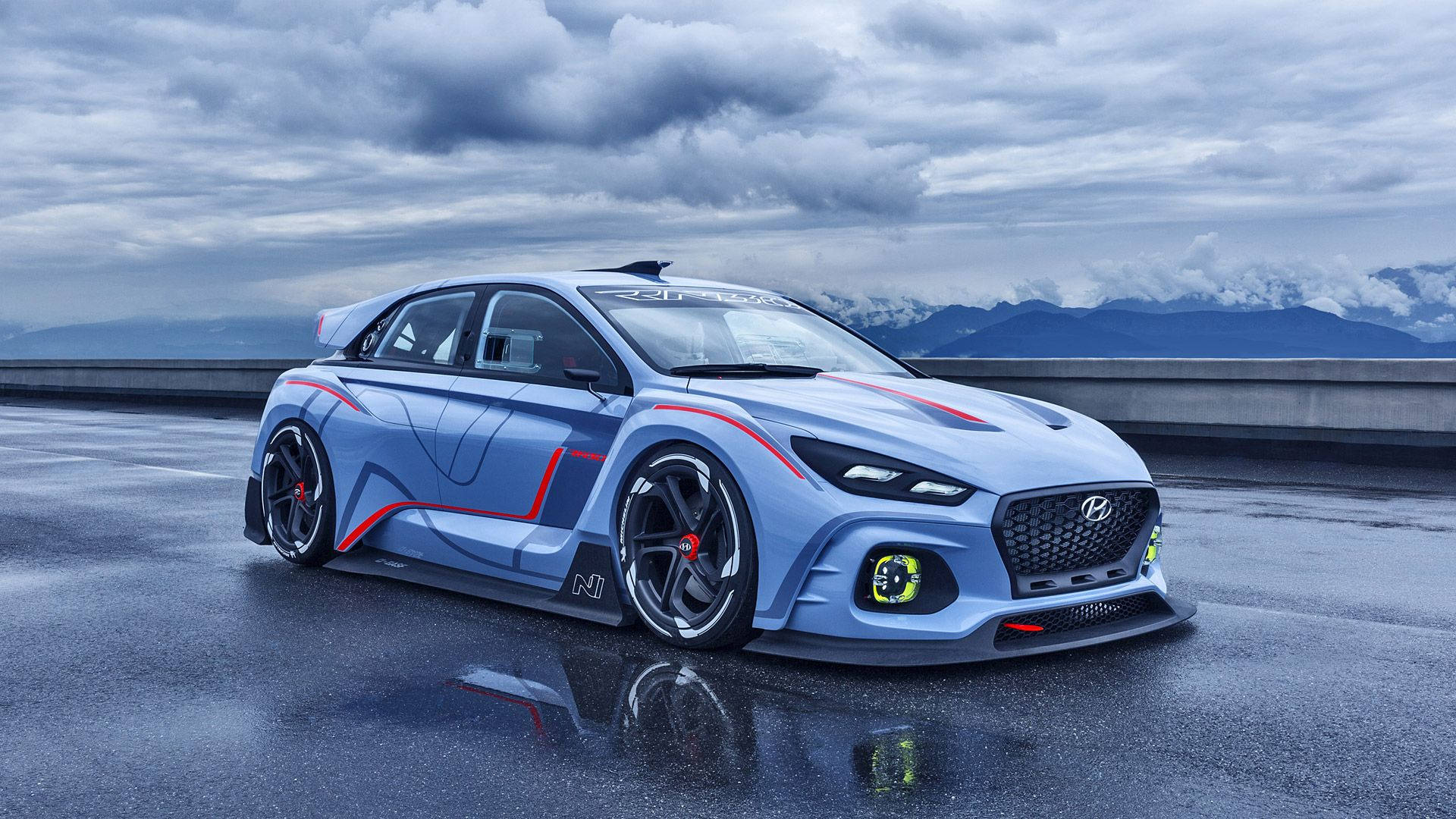 Hyundai 桌布 壁紙 — 一輛時尚的藍色現代N賽車帶有紅色點綴，停在潮濕的道路上，在陰天和遠處山脈的背景下反射出其大膽的設計。