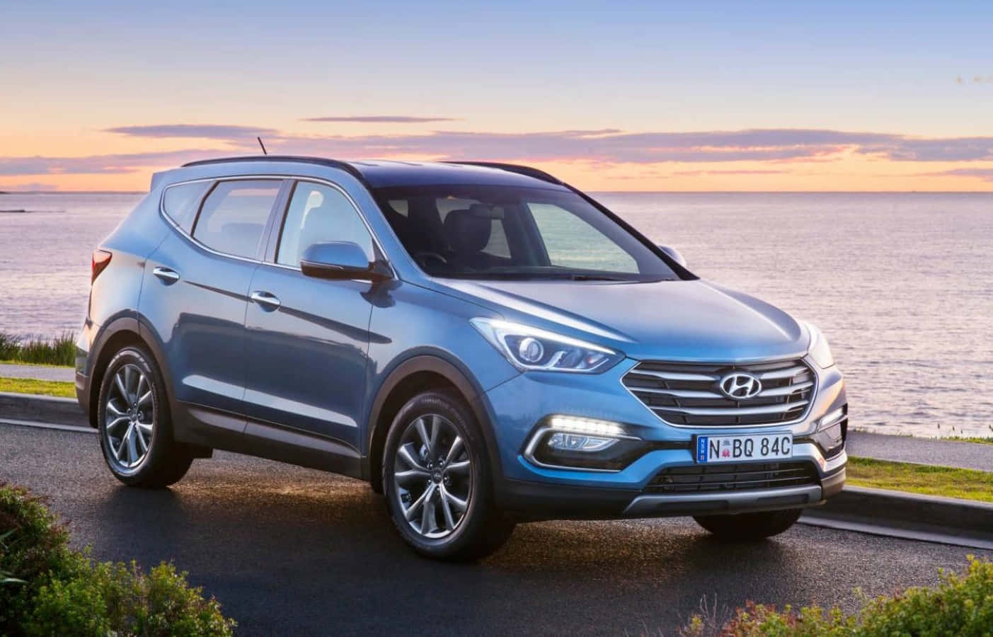 Hyundai 桌布 壁紙 — 一輛時尚的藍色現代SUV在日落時分停在海邊，水面平靜，天空呈現柔和的橙色。