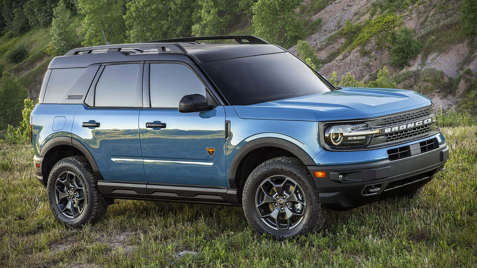 Ford Bronco 桌布 壁紙 — 一輛時尚的藍色福特Bronco SUV停在草地上，背景有岩石山丘和綠樹。