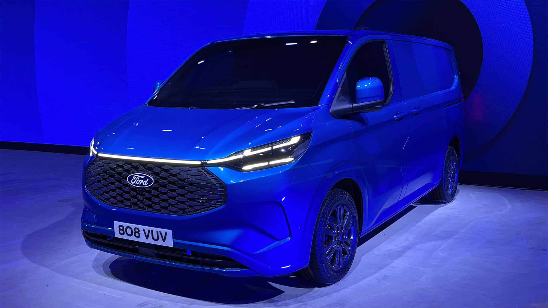 Ford Transit 桌布 壁紙 — 一輛時尚的藍色福特廂型車在產品發表會的戲劇性舞台燈光下閃閃發光。
