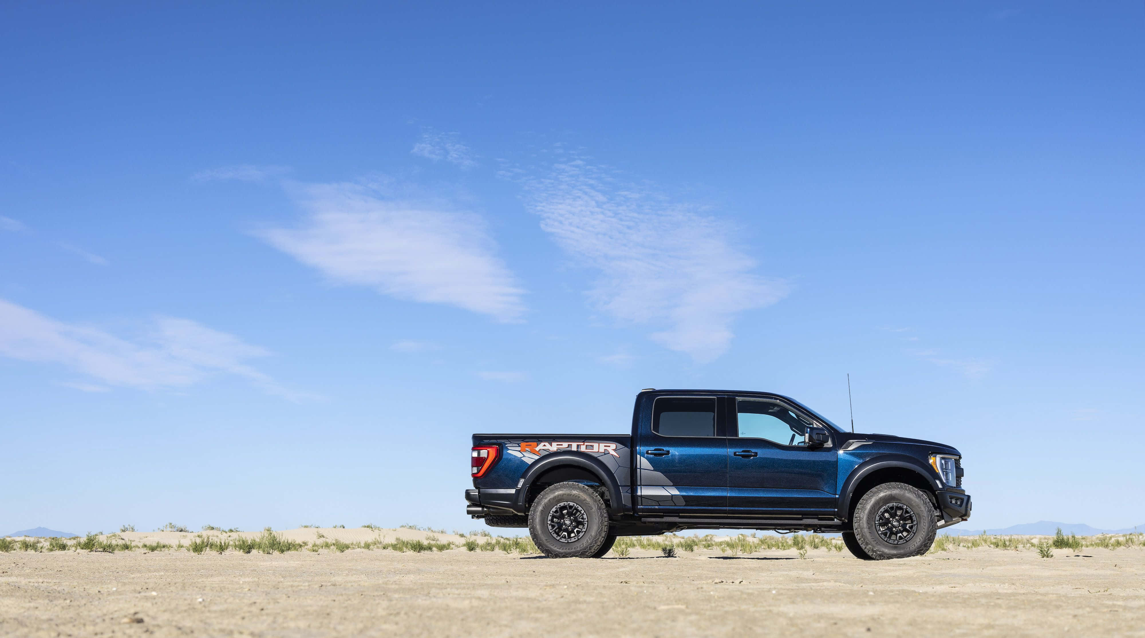 Ford F 150 桌布 壁紙 — 一輛時尚的藍色福特猛禽貨車在廣闊的沙漠平原上，在晴朗的藍天和薄雲下矗立。