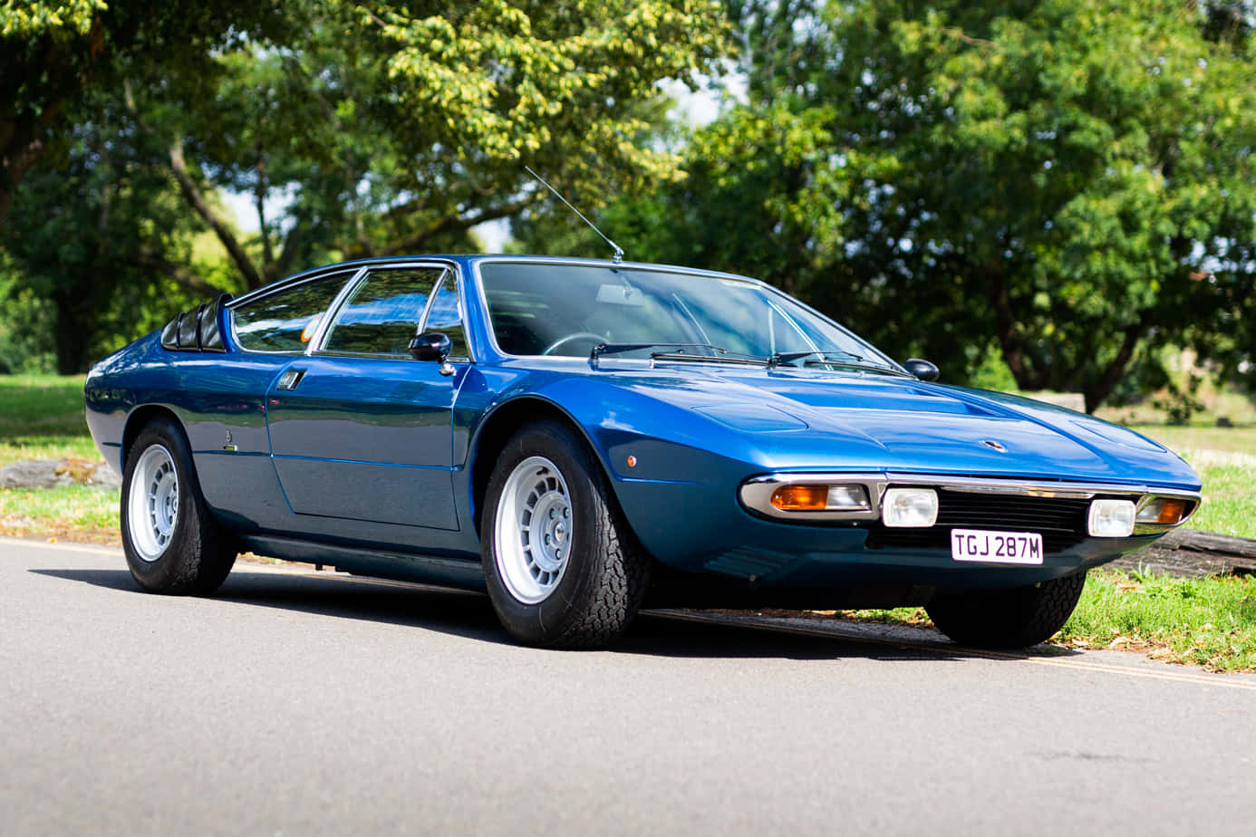 Lamborghini Urraco 桌布 壁紙 — 一輛時尚的藍色經典跑車停泊在林蔭大道上，沐浴在明亮的日光下。