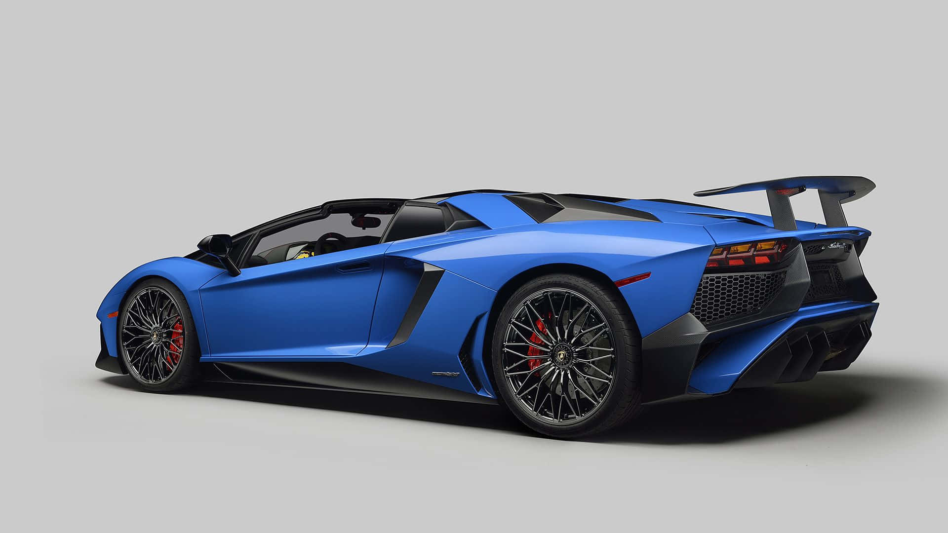 跑車 桌布 壁紙 — 一輛時尚的藍色藍寶堅尼 Aventador SVJ 敞篷跑車，帶有黑色飾件和紅色制動卡鉗，在純灰色工作室背景前以側面展示。