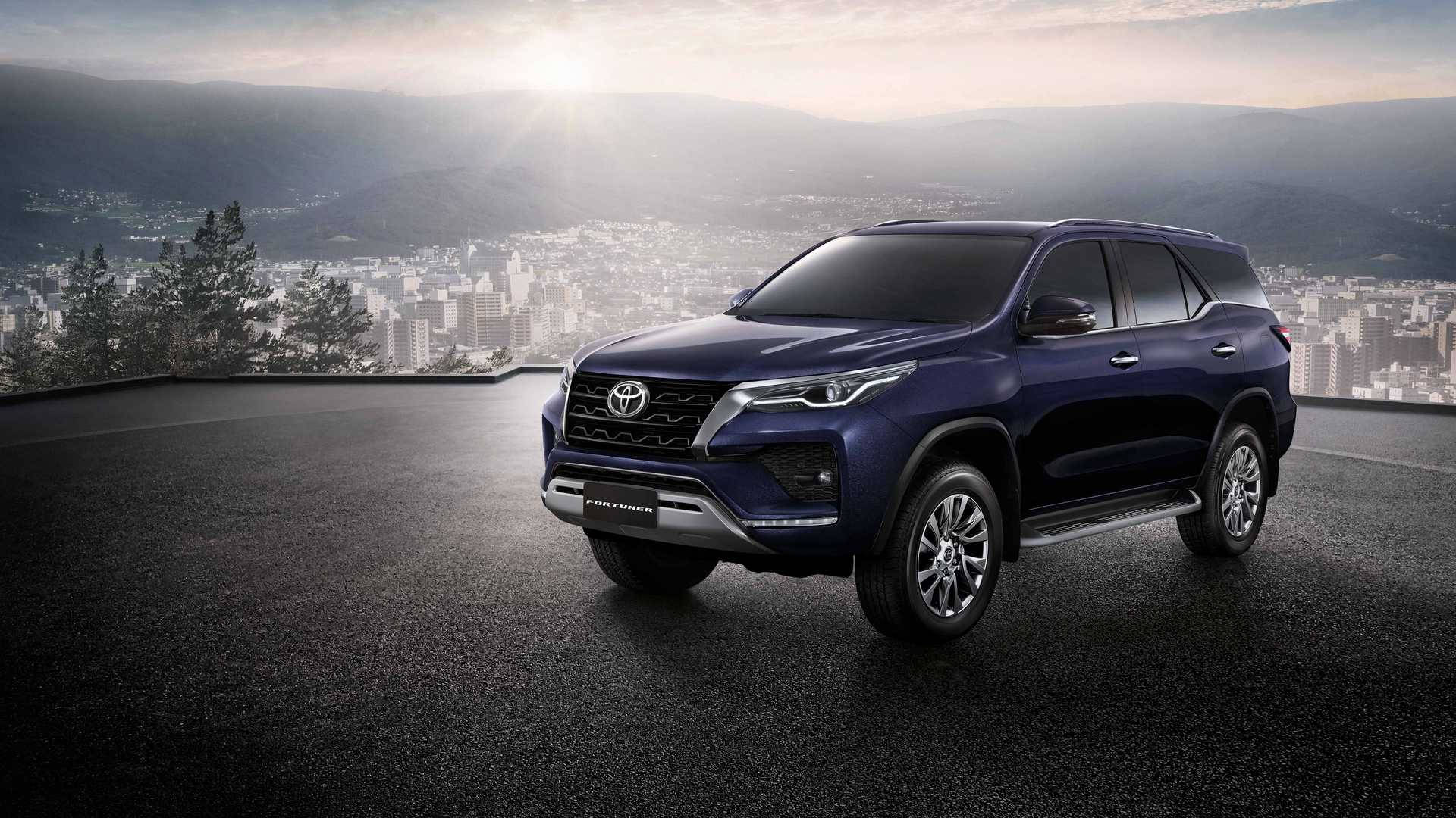 藍色豐田 Fortuner SUV 停泊在屋頂，俯瞰日出時的城市與山巒。 — Toyota Supra Mk4 壁紙
