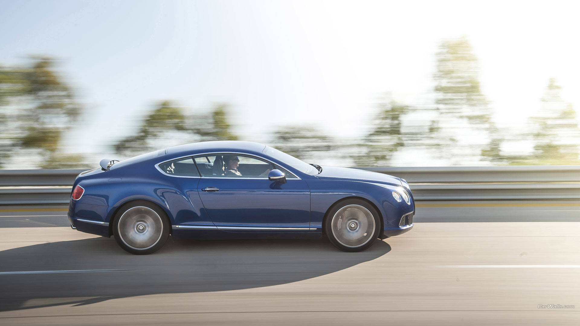 bentley HD 桌布 壁紙 — 一輛時尚的藍色賓利 Continental GT 在陽光明媚的高速公路上疾馳，背景是模糊的綠樹。
