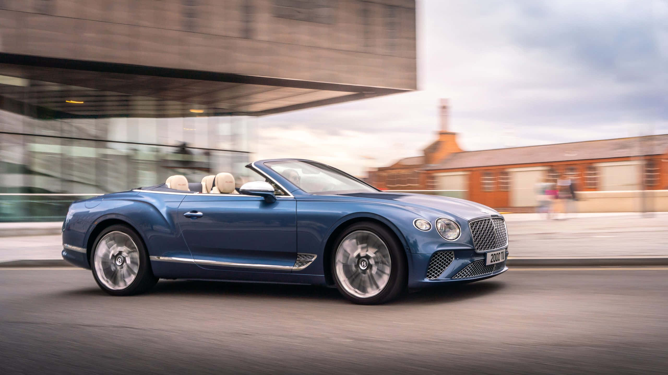 Bentley Continental Gt 桌布 壁紙 — 一輛時尚的藍色賓利敞篷車在現代城市街道上奔馳，背景呈現動態模糊效果。