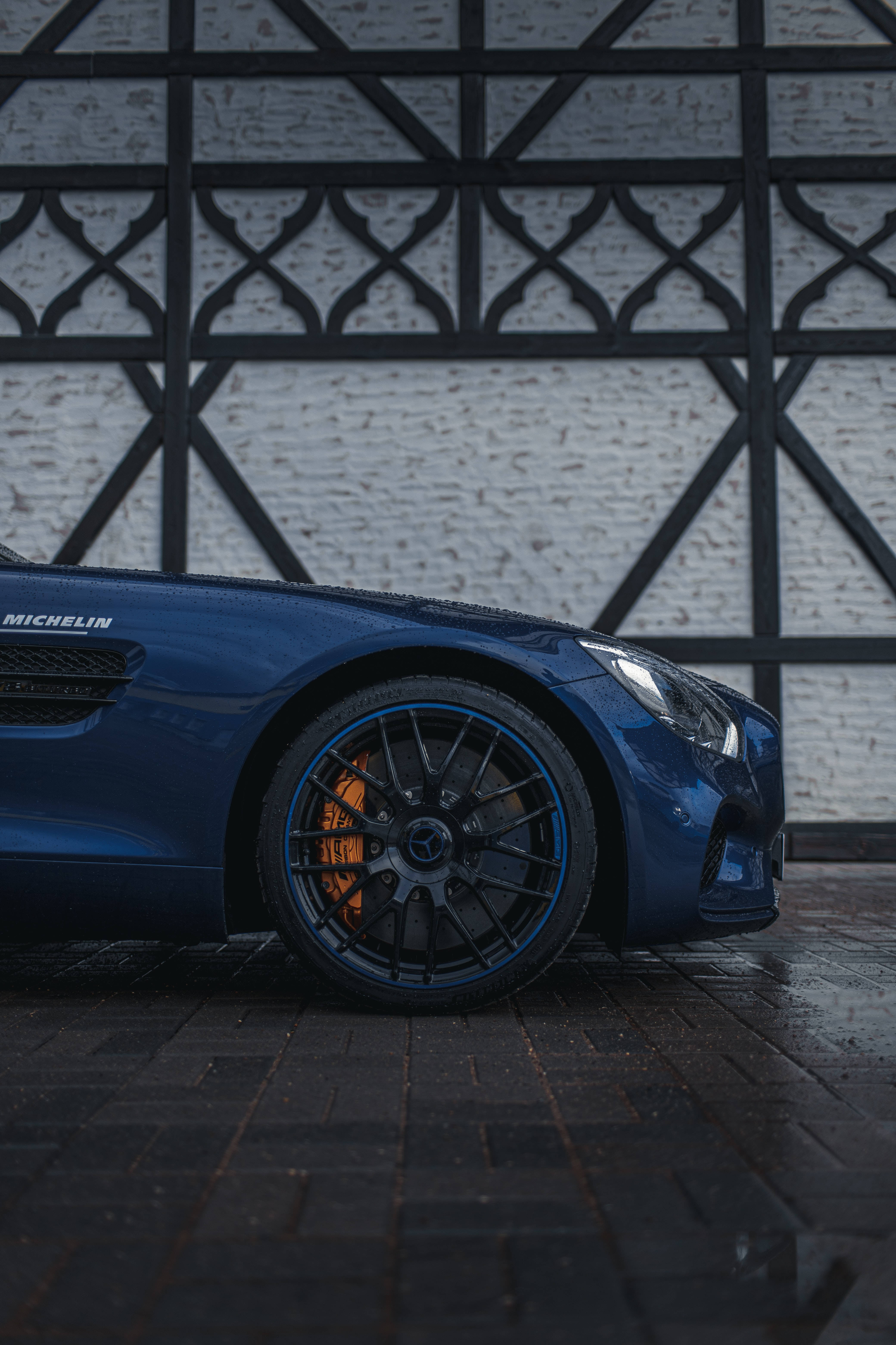Mercedes 桌布 壁紙 — 一輛時尚的藍色跑車，帶有發光的橙色煞車，停放在濕漉漉的路面上，背景是黑色幾何牆。