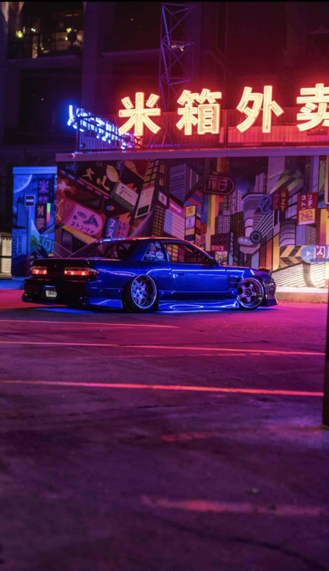 JDM iPhone 桌布 壁紙 — 一輛時尚的藍色跑車在夜晚充滿活力的城市街道上，在霓虹燈下閃耀。