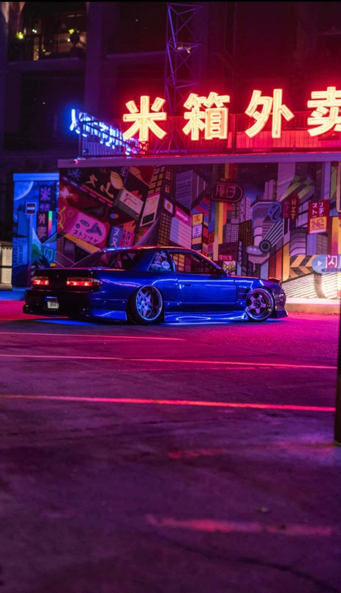 JDM 桌布 壁紙 — 一輛時尚的藍色跑車在夜間充滿活力的城市街道上，在霓虹燈下閃耀。