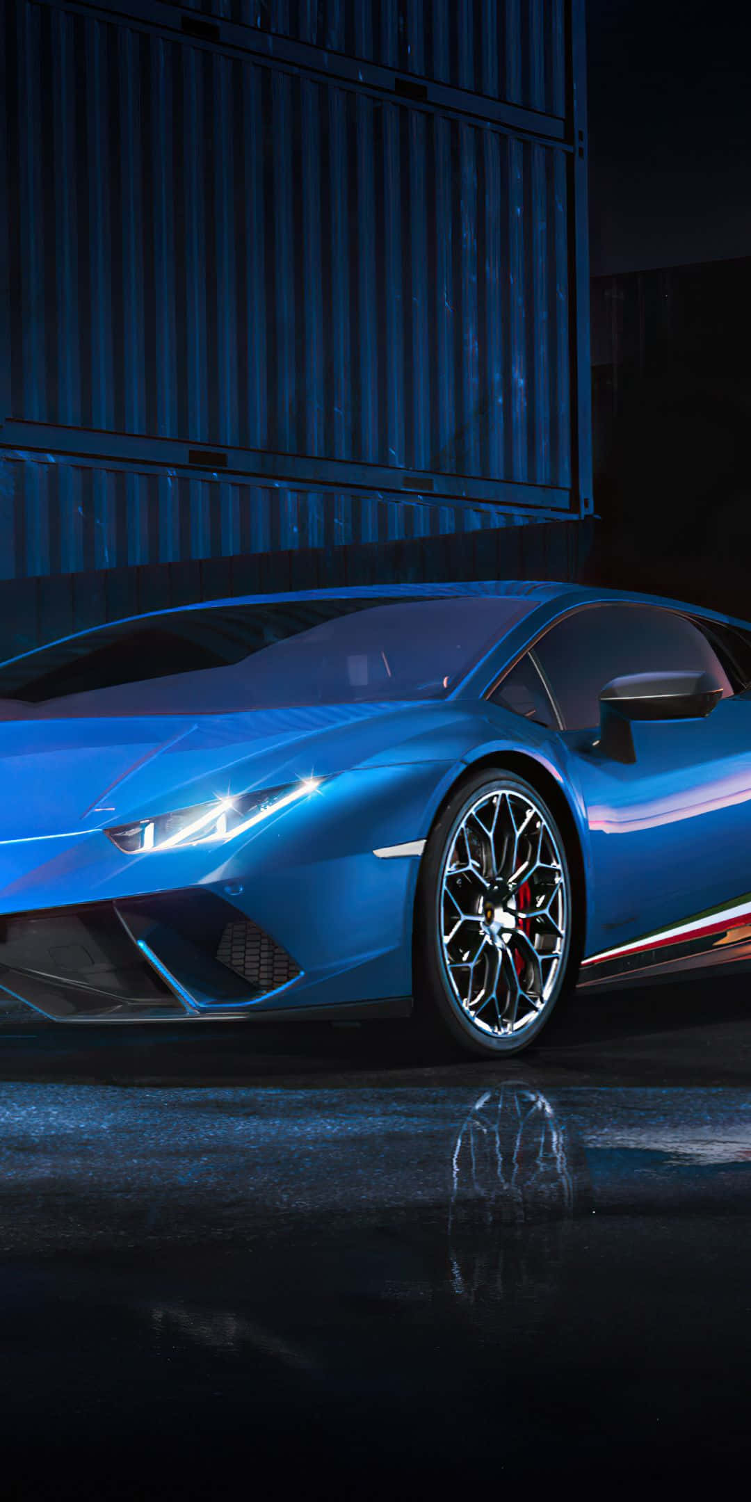 Pixel 3 Lamborghini 桌布 壁紙 — 一輛時尚的藍色跑車在戲劇性燈光下閃耀，背景是黑暗的工業環境，地面潮濕且具有反射性。