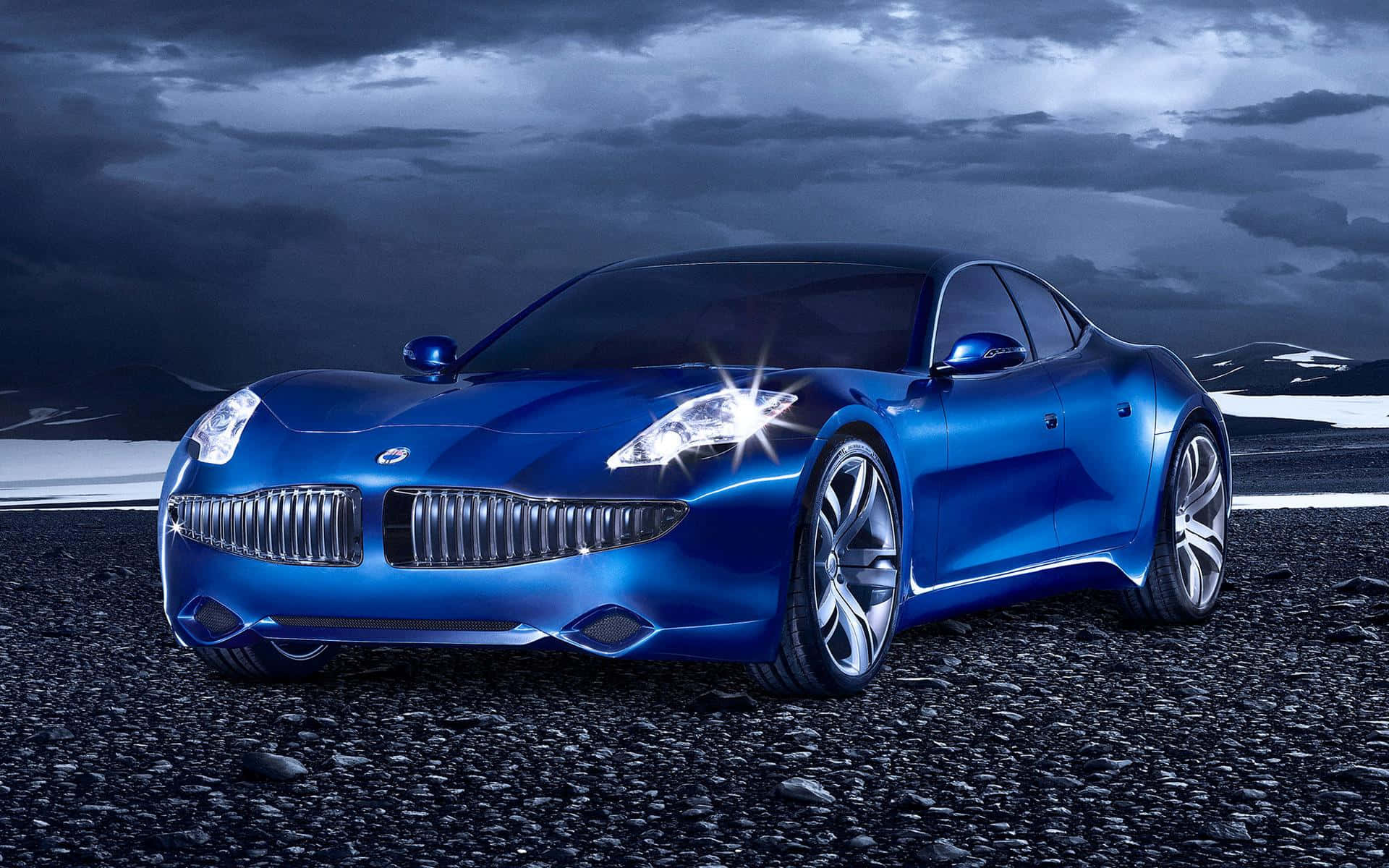 Fisker 桌布 壁紙 — 一輛時尚的藍色跑車在戲劇性的暴風雲下，在碎石平原上閃閃發光，遠處有雪山。