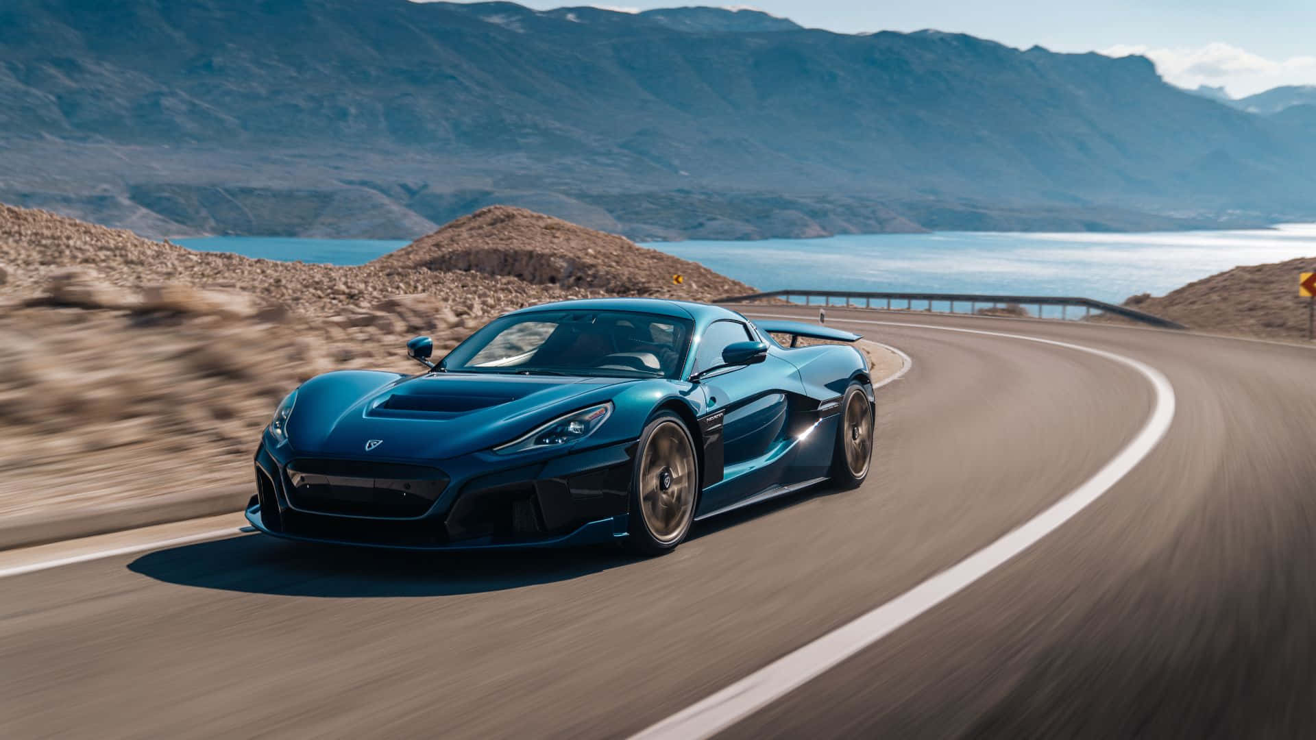 Rimac 桌布 壁紙 — 一輛時尚的藍色跑車在明亮的日光下，沿著蜿蜒的山路，在平靜的湖邊飛馳。