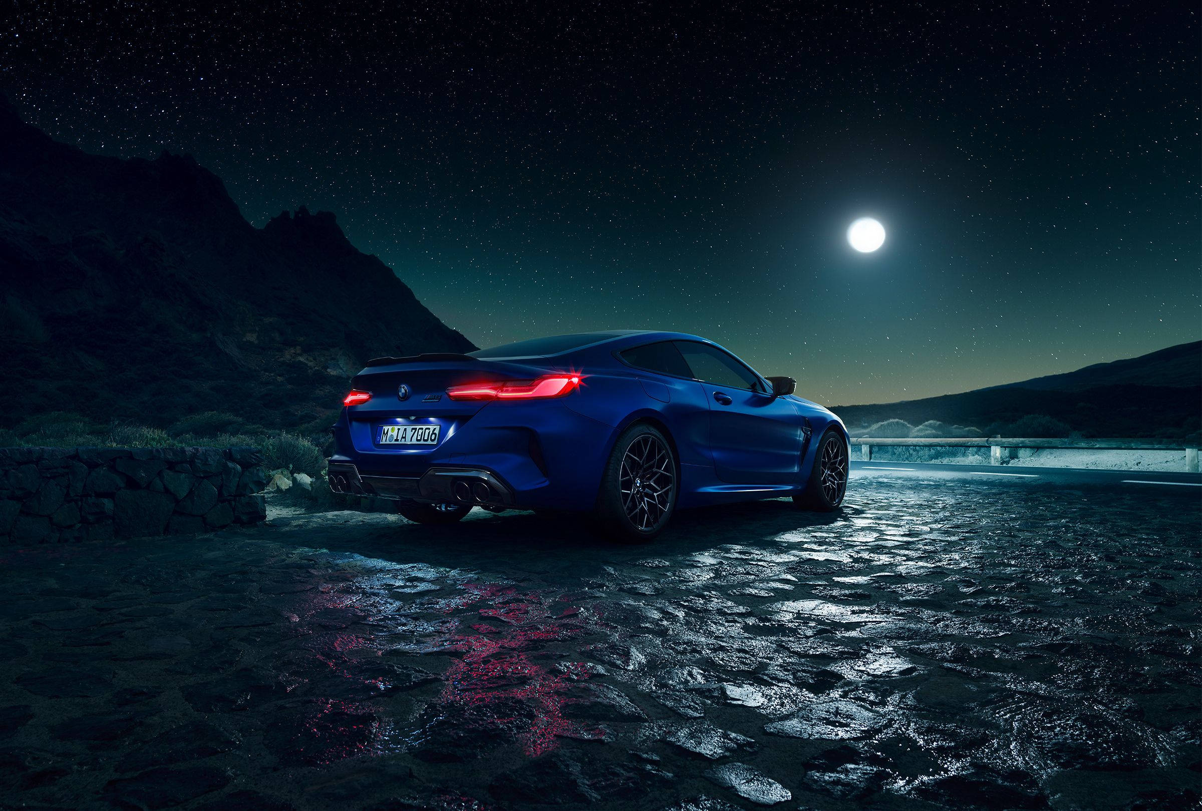 BMW 動圖 桌布 壁紙 — 一輛時尚的藍色跑車在滿月下，夜晚的濕滑鵝卵石路上閃耀，背景是星空和山脈。
