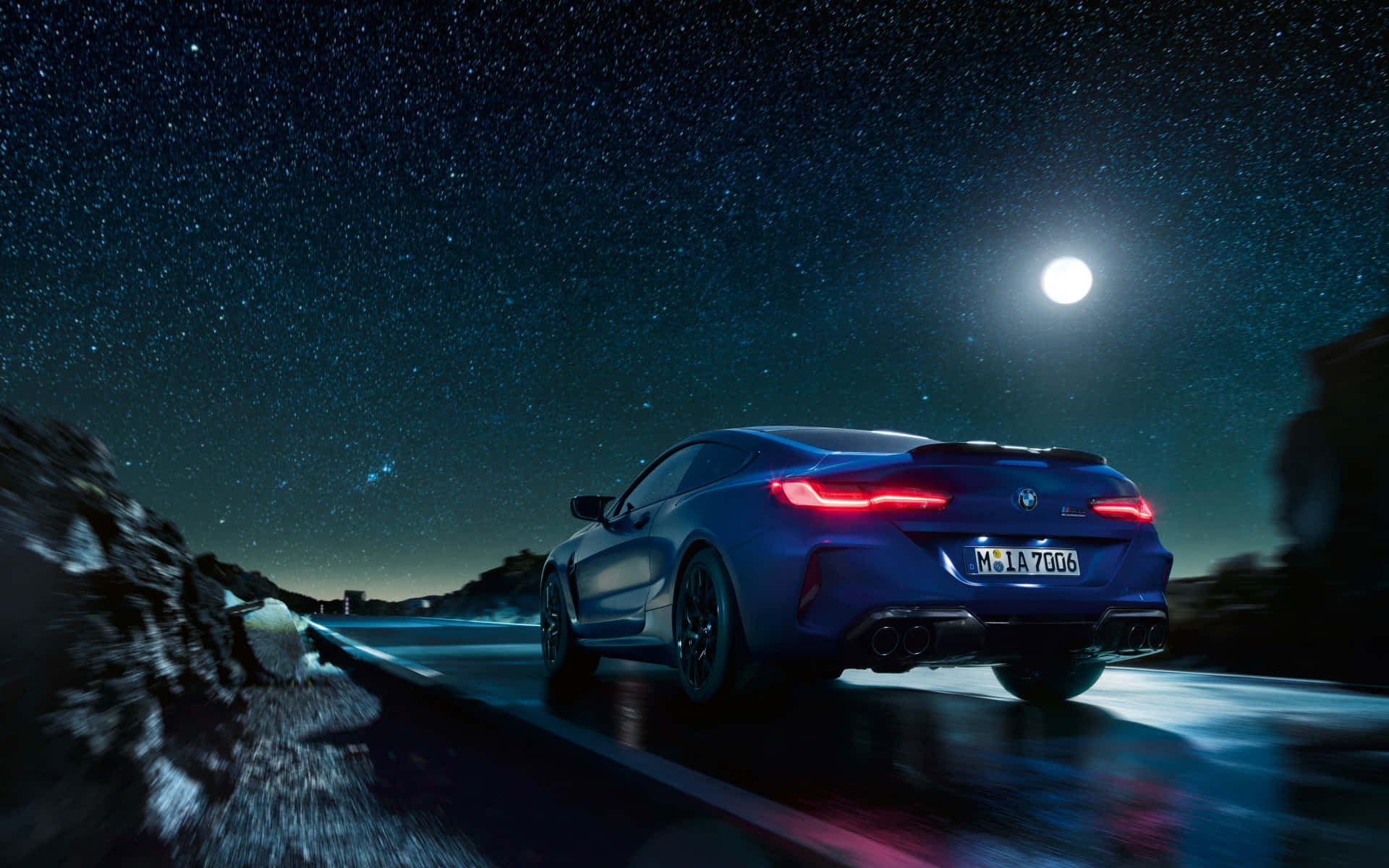 Bmw M8 4K 桌布 壁紙 — 一輛時尚的藍色跑車在繁星點點的夜空下行駛，明亮的月亮高懸在蜿蜒的山路上方。