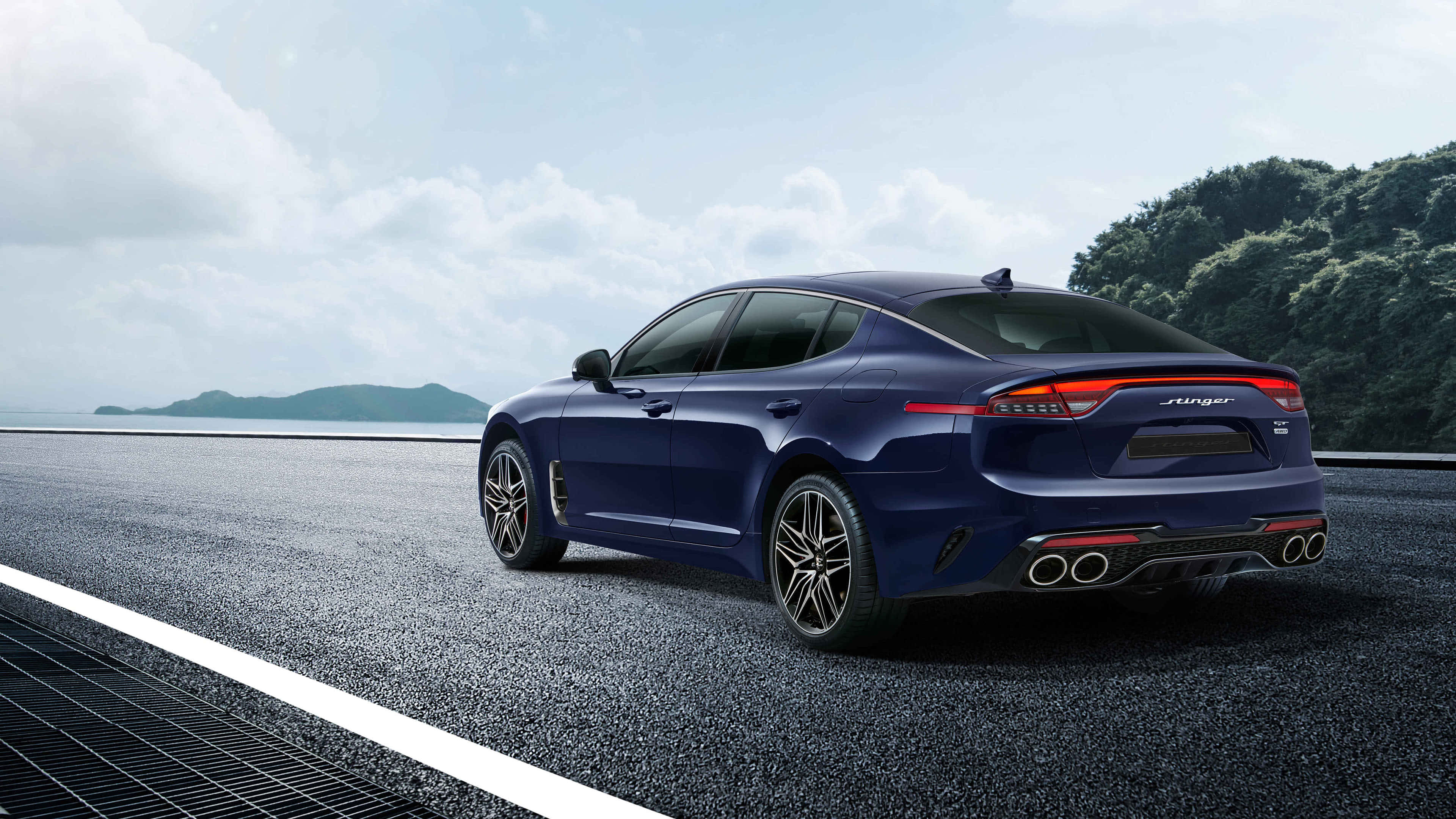 Kia Stinger 桌布 壁紙 — 一輛時尚的藍色跑車配備四個排氣管，在部分多雲的天空下行駛在沿海公路上。