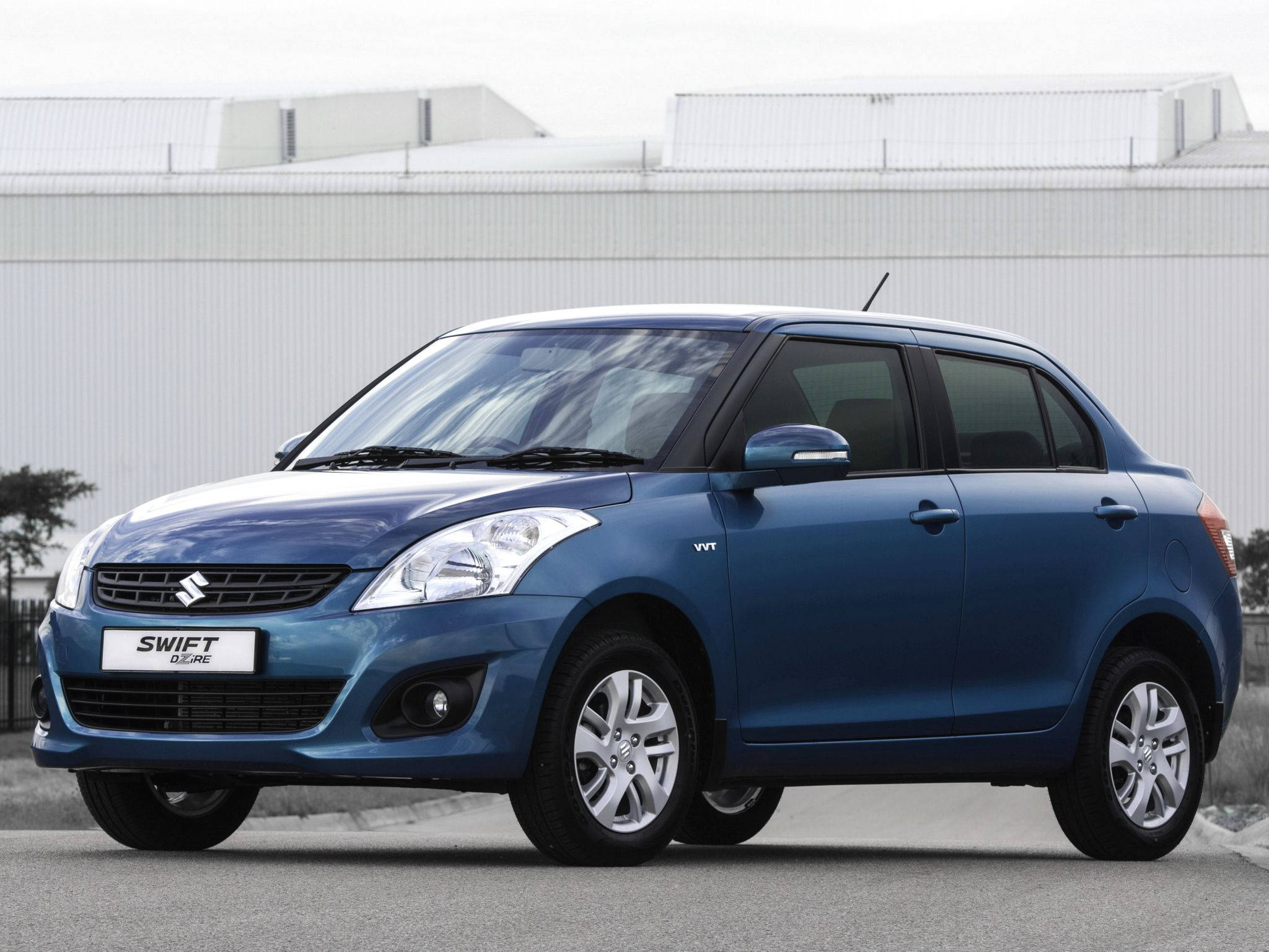 Suzuki 桌布 壁紙 — 一輛時尚的藍色鈴木 Swift Glance 轎車停在柏油路上，背景是現代工業建築。