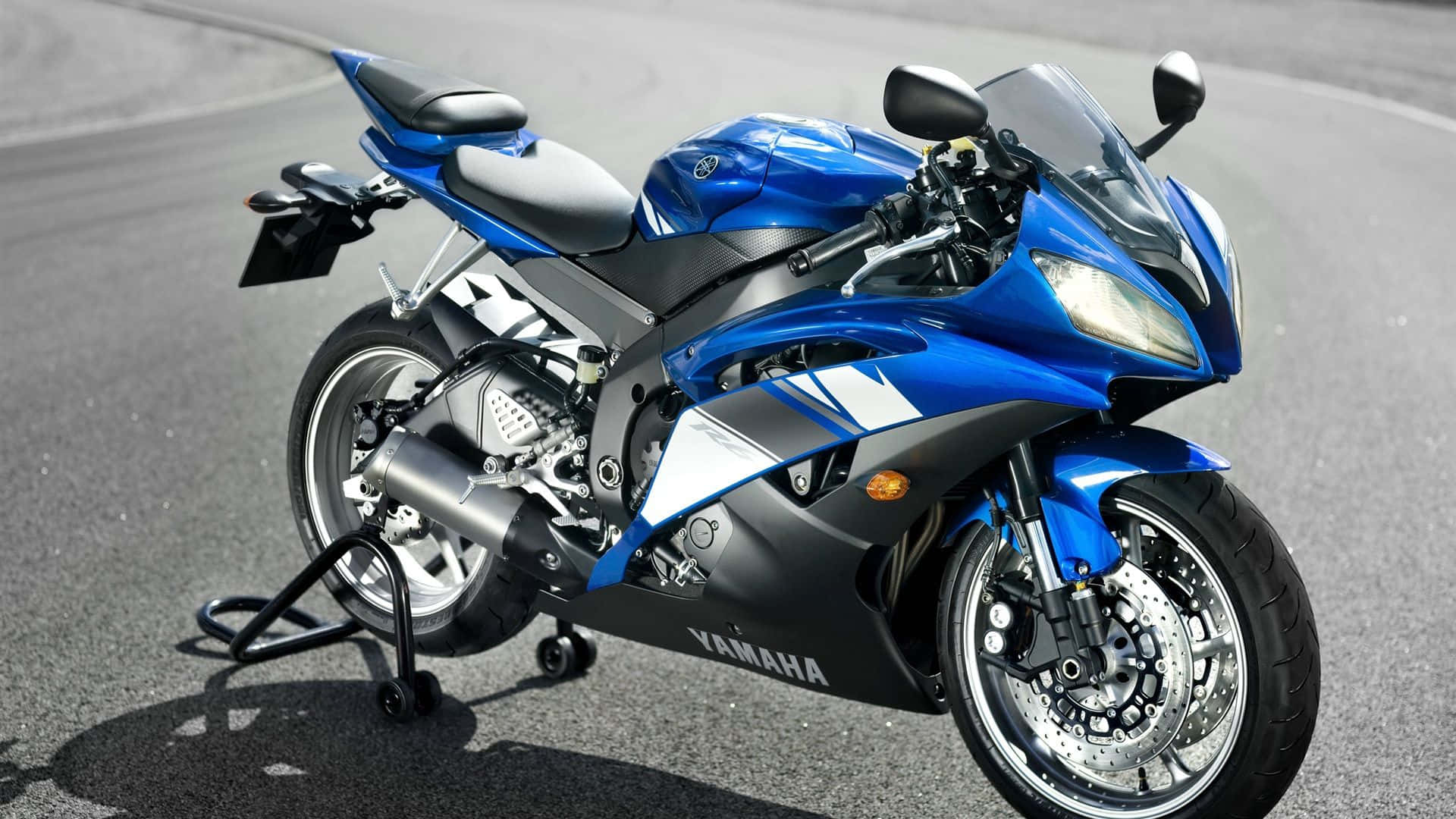機車 桌布 壁紙 — 一輛時尚的藍黑配色Yamaha運動機車在明亮的日光下停放在柏油路面上。