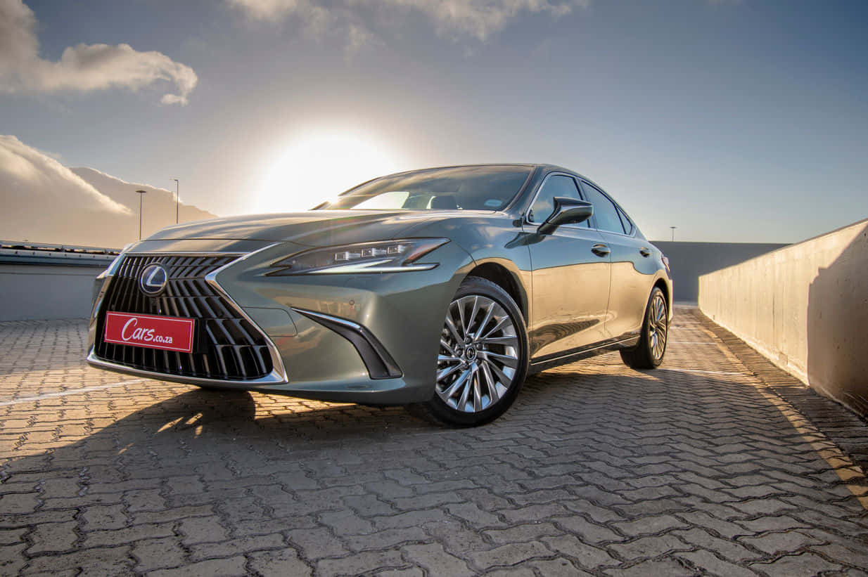 Lexus Es 300h 桌布 壁紙 — 一輛時尚的金屬綠色Lexus轎車在金色日出光下閃耀，停泊在鋪砌的屋頂上，遠山為背景。