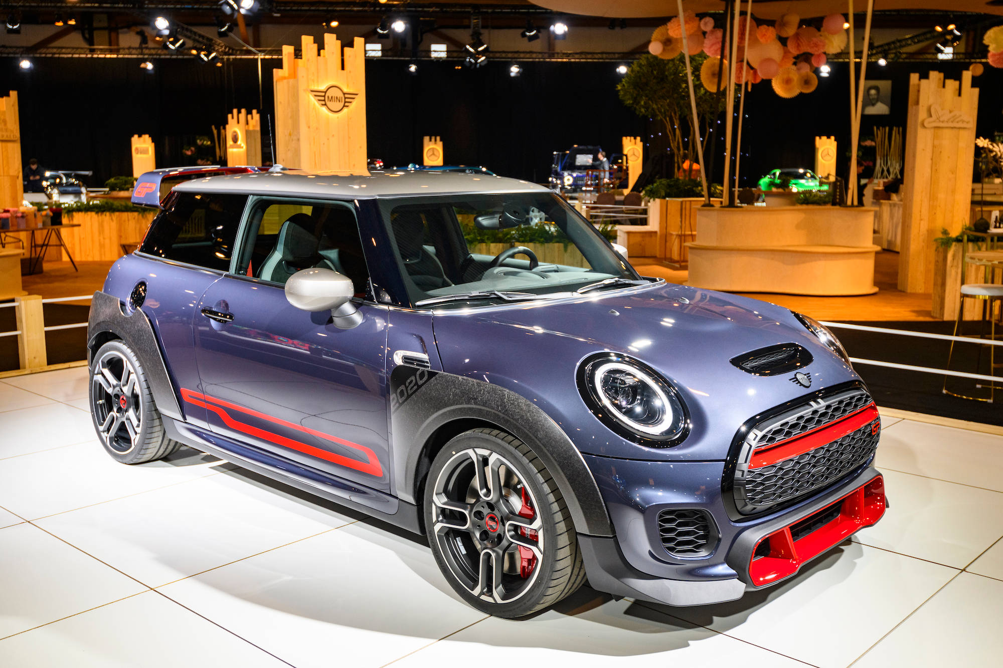 Mini 桌布 壁紙 — 一輛時尚的金屬藍色MINI Cooper JCW，帶有紅色點綴，在白色瓷磚地板上閃耀著明亮的展覽燈光。