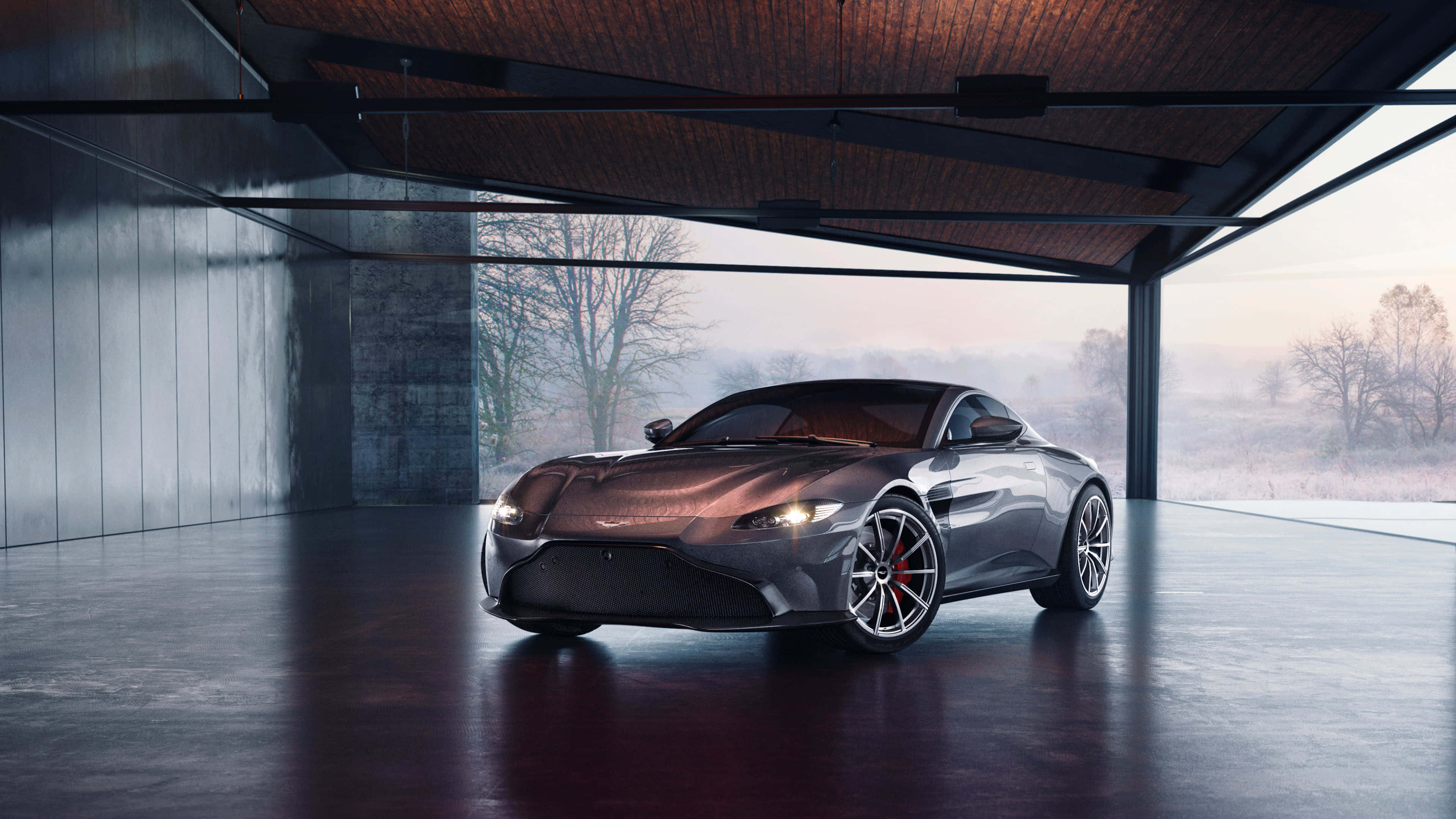 Aston Martin Vantage 桌布 壁紙 — 一輛時尚的金屬跑車在現代玻璃牆車庫內，於柔和晨光下閃耀，外面有霧濛濛的冬季樹木。