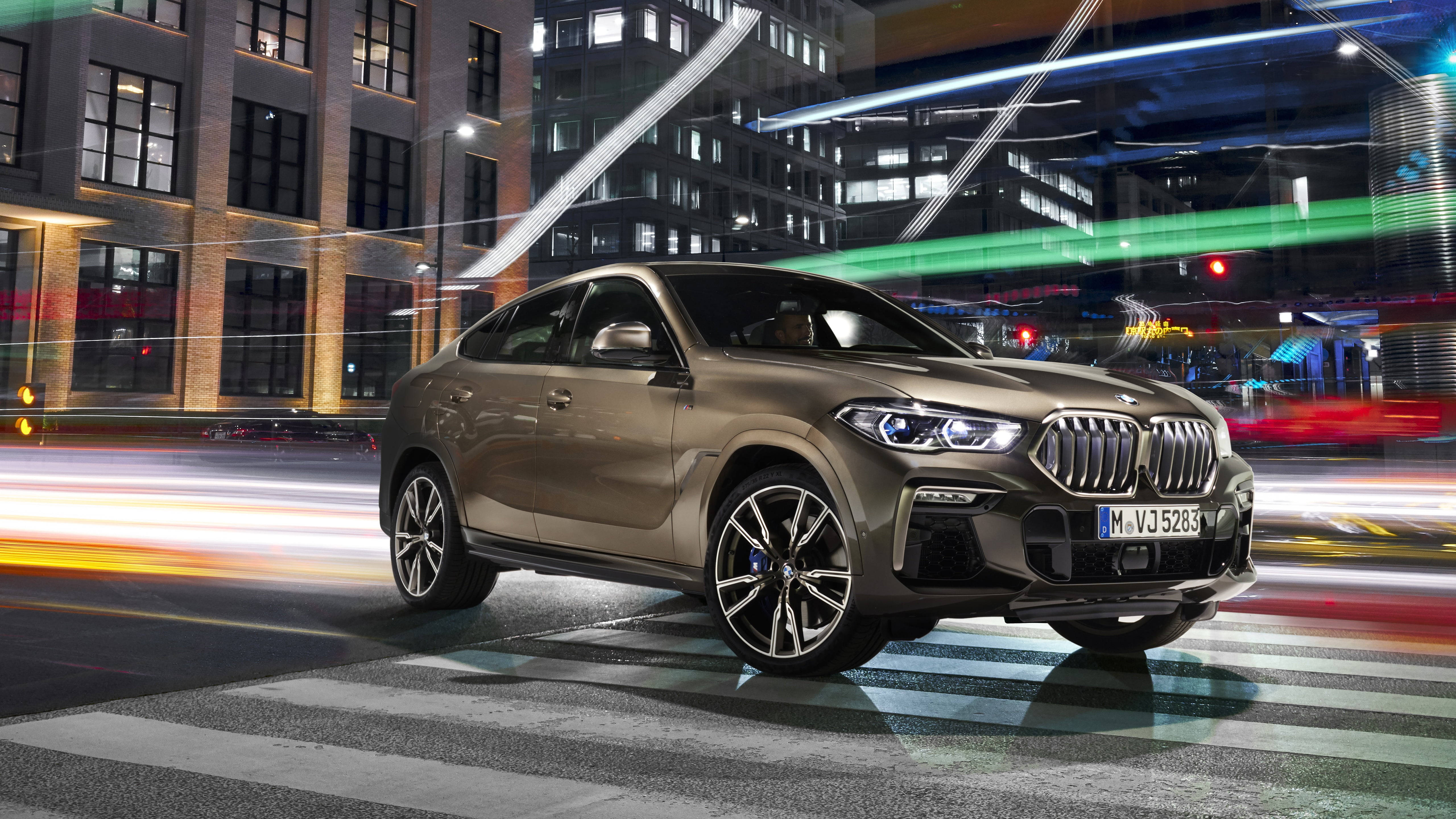 m 桌布 壁紙 — 一輛時尚的金色BMW X6 SUV在夜晚穿過充滿活力的城市街道，身後是霓虹燈光和模糊的車流。