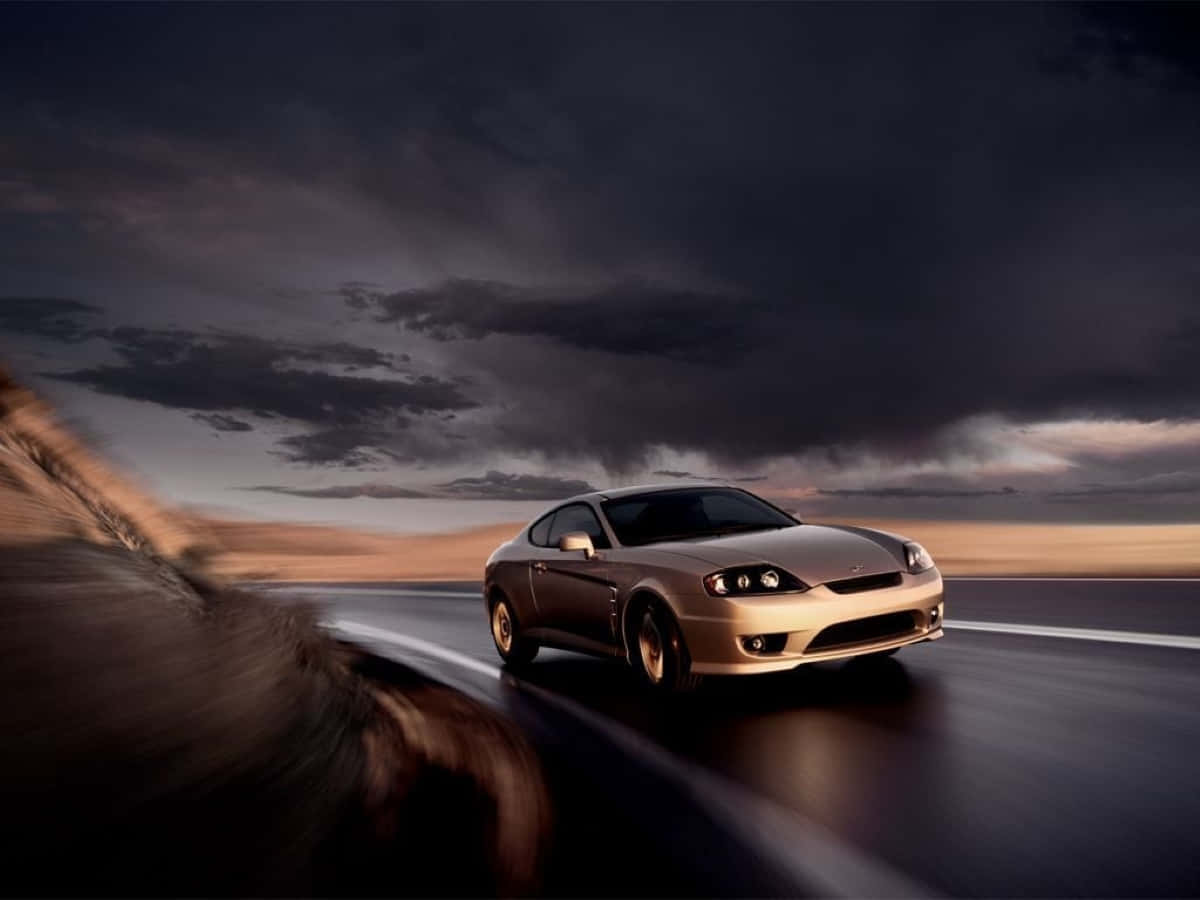 Hyundai Tiburon 桌布 壁紙 — 一輛時尚的金色跑車在黃昏時分，在戲劇性的暴風雨天空下，在潮濕的道路上疾馳。