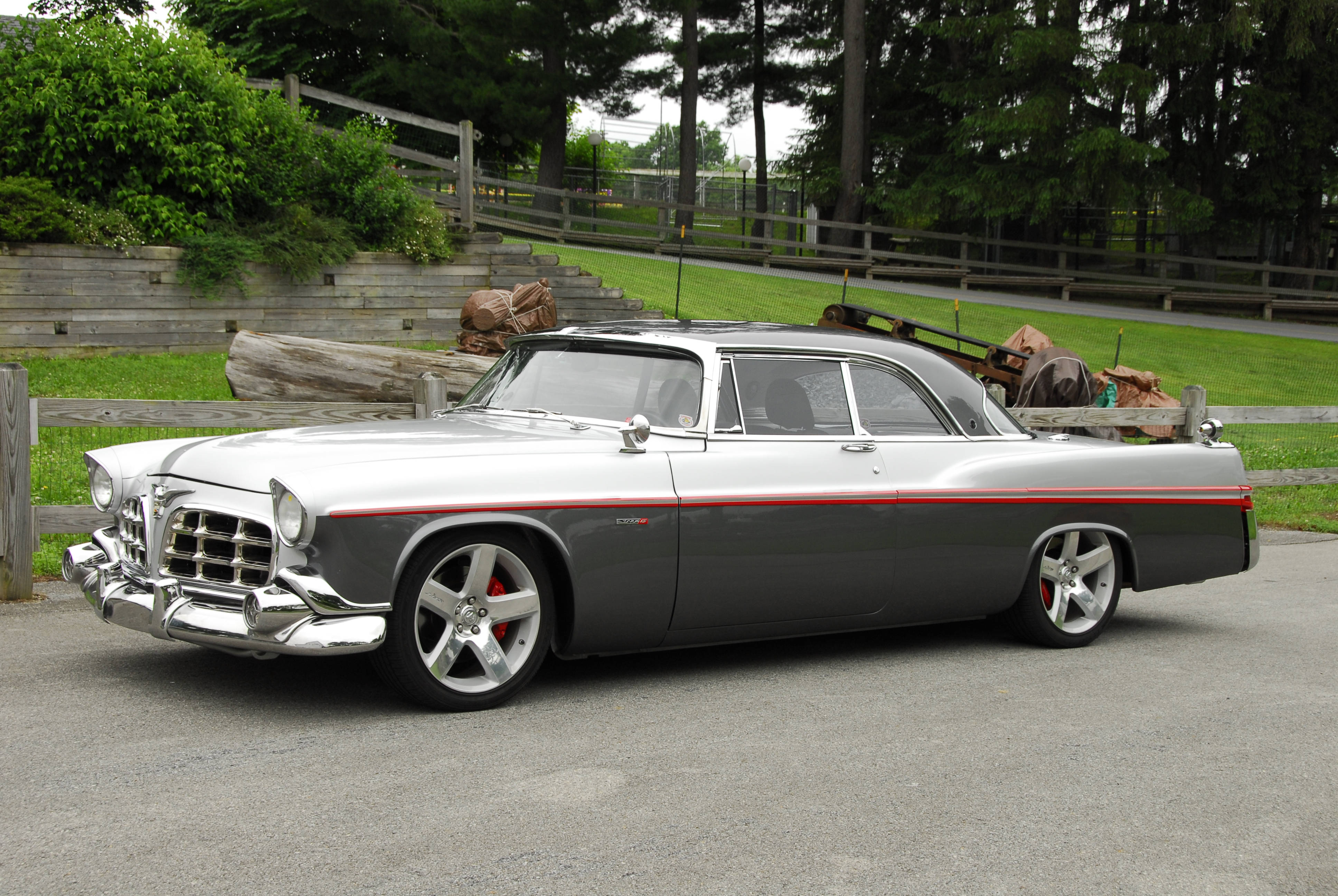 Chrysler 桌布 壁紙 — 一輛時尚的銀灰色經典汽車，帶有紅色飾邊和定制輪圈，停在木柵欄和綠植旁的碎石車道上。