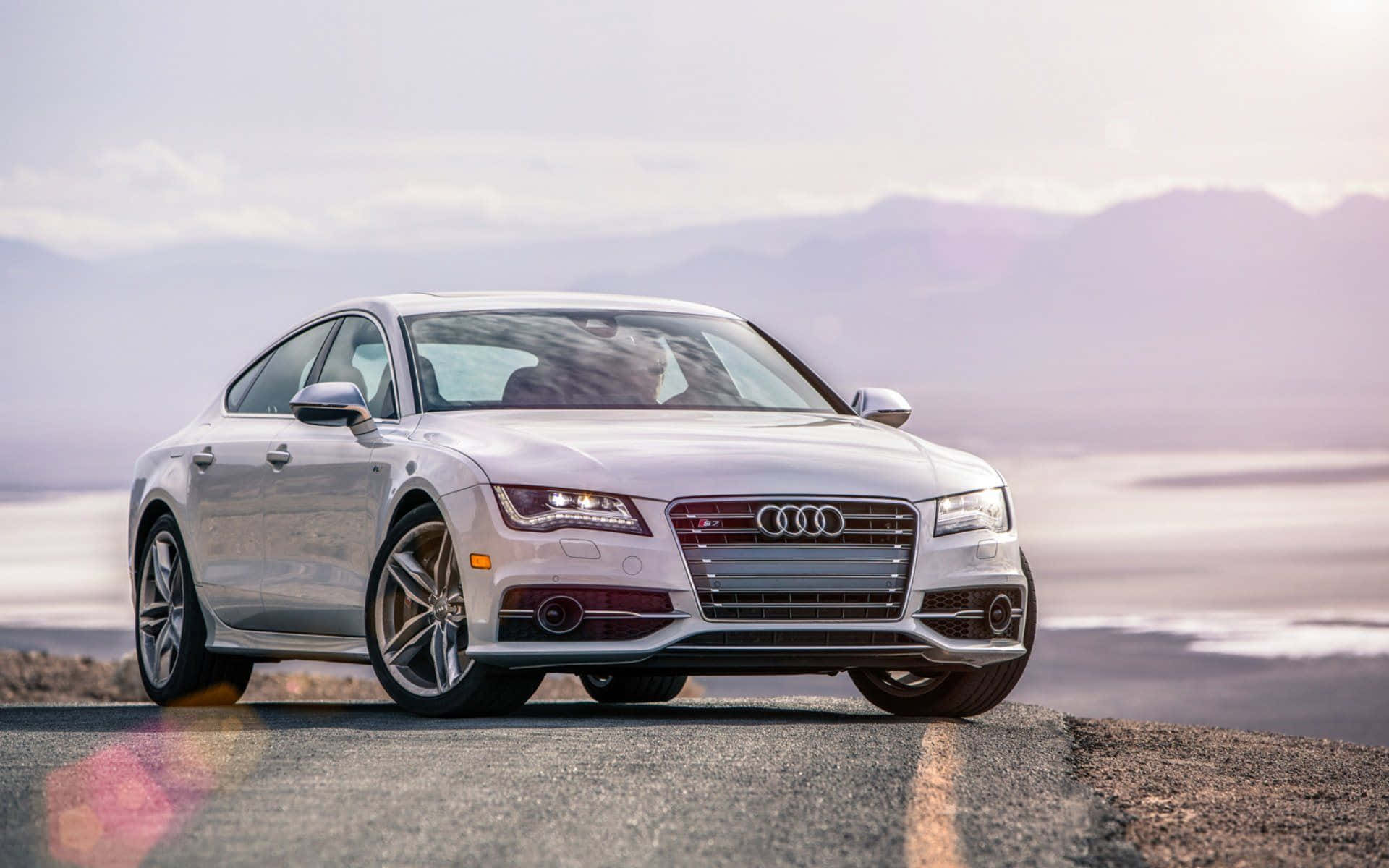 Audi S7 桌布 壁紙 — 一輛時尚的銀色 Audi 房車停在沙漠公路上，遠山在柔和的暮色天空下。