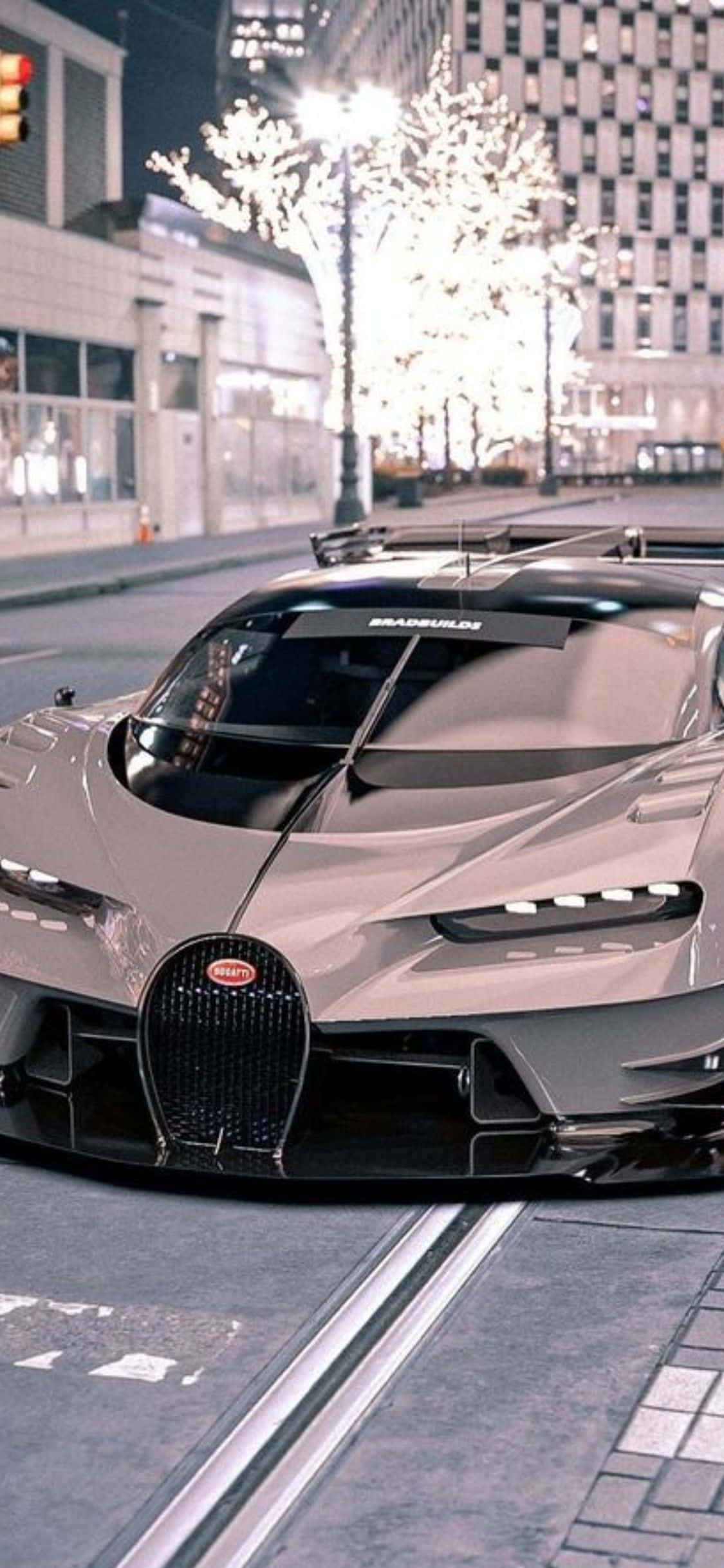 iPhone Xs Bugatti 桌布 壁紙 — 一輛時尚的銀色 Bugatti 超跑停在夜晚的城市街道上，背景是燈光璀璨的樹木和現代建築。