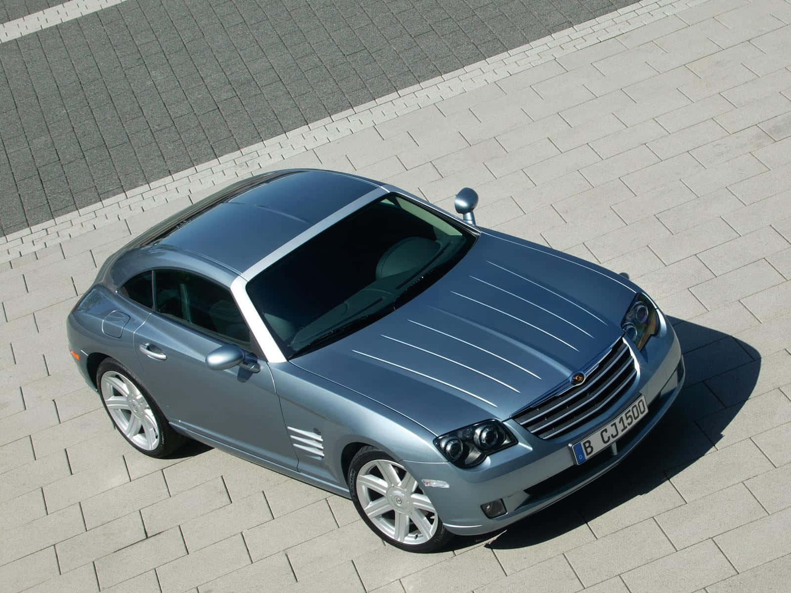 Chrysler Crossfire 桌布 壁紙 — 一輛時尚的銀色 Chrysler Crossfire 跑車停放在淺灰色磚砌路面上，在明亮的日光下。