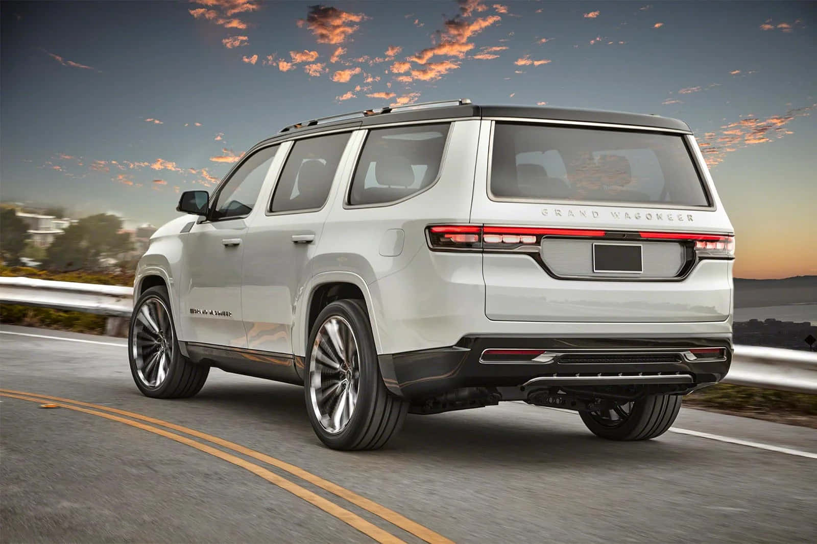 Jeep Wagoneer 桌布 壁紙 — 一輛時尚的銀色 Grand Wagoneer SUV 沿著海岸公路在日落時分巡航，頭頂是鮮豔的橙色雲彩。