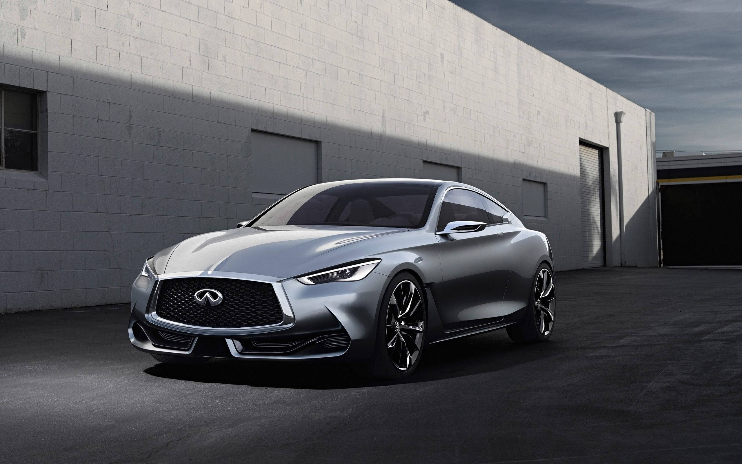 Infiniti 桌布 壁紙 — 一輛時尚的銀色 Infiniti 跑車停放在 stark 白色磚砌倉庫前，在戲劇性的燈光下。