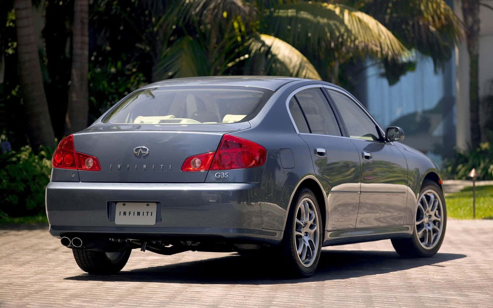 Infiniti G35 桌布 壁紙 — 一輛時尚的銀色 Infiniti G35 轎車停放在陽光普照的磚砌車道上，背景有棕櫚樹和茂密的綠植。