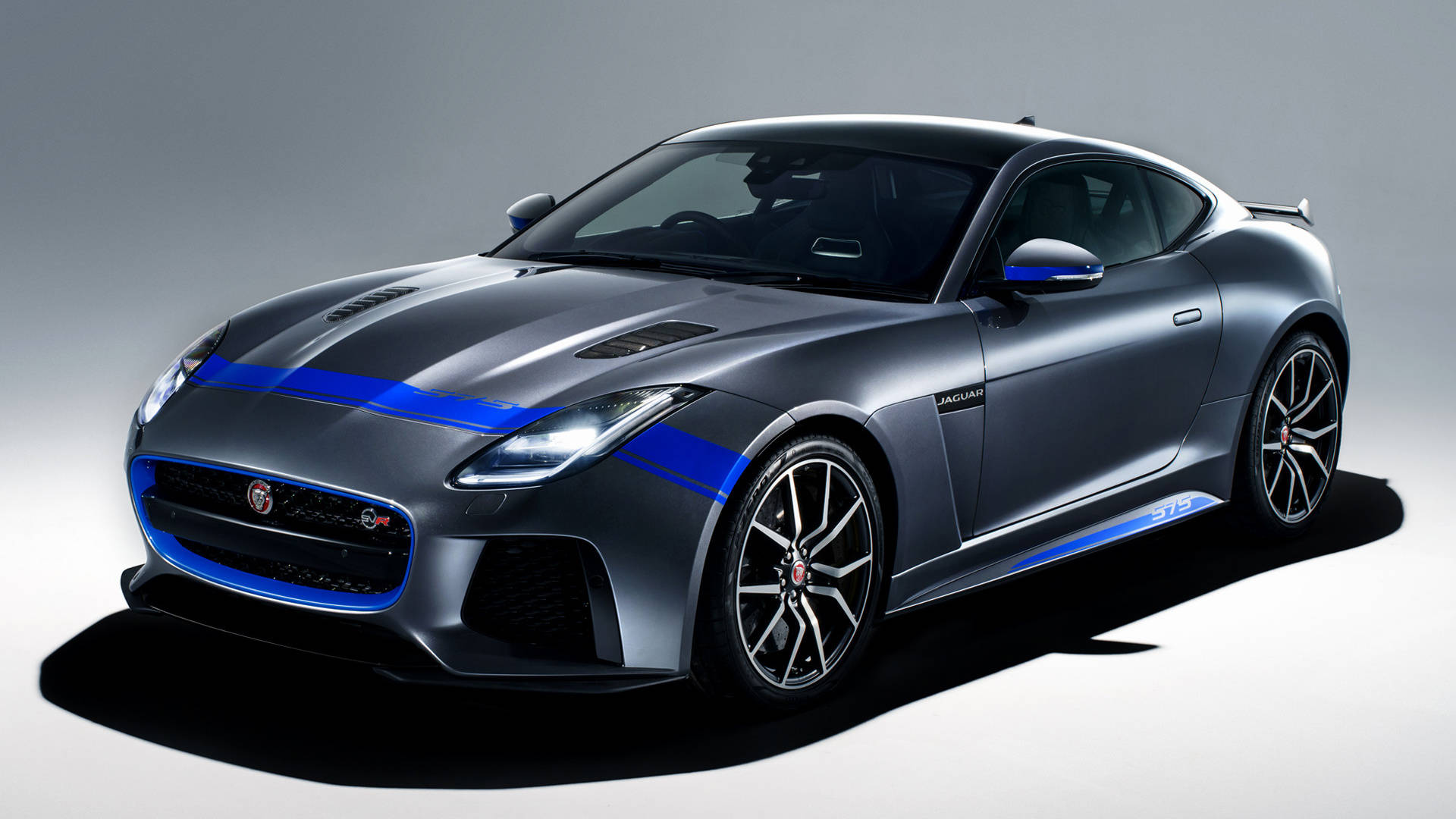 圖形 桌布 壁紙 — 一輛時尚的銀色 Jaguar F-Type 跑車，帶有醒目的藍色賽車條紋和黑色輪圈，以極簡灰色工作室背景為襯托。