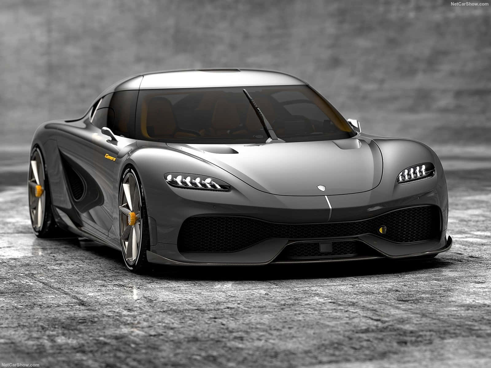 Koenigsegg 桌布 壁紙 — 一輛時尚的銀色 Koenigsegg Jesko 超跑帶有黃色點綴，停放在紋理混凝土車庫地板上，背景是灰色磚牆。