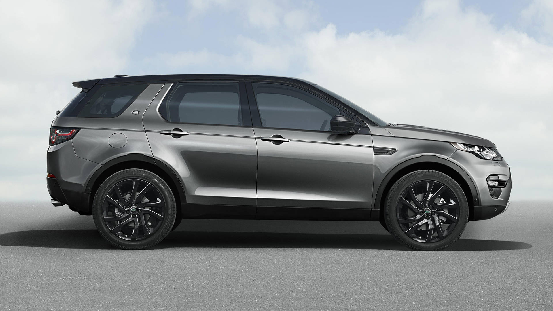land rover iPhone 桌布 壁紙 — 一輛時尚的銀色 Land Rover Discovery Sport 帶有黑色飾件，在陰天之下立於灰色表面上。